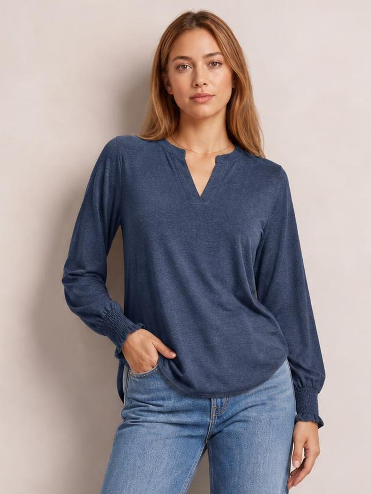 A model poses in a navy blue notched long sleeve T-shirt with a relaxed silhouette, V-neckline, delicate ruffled cuffs, and slight stretch.