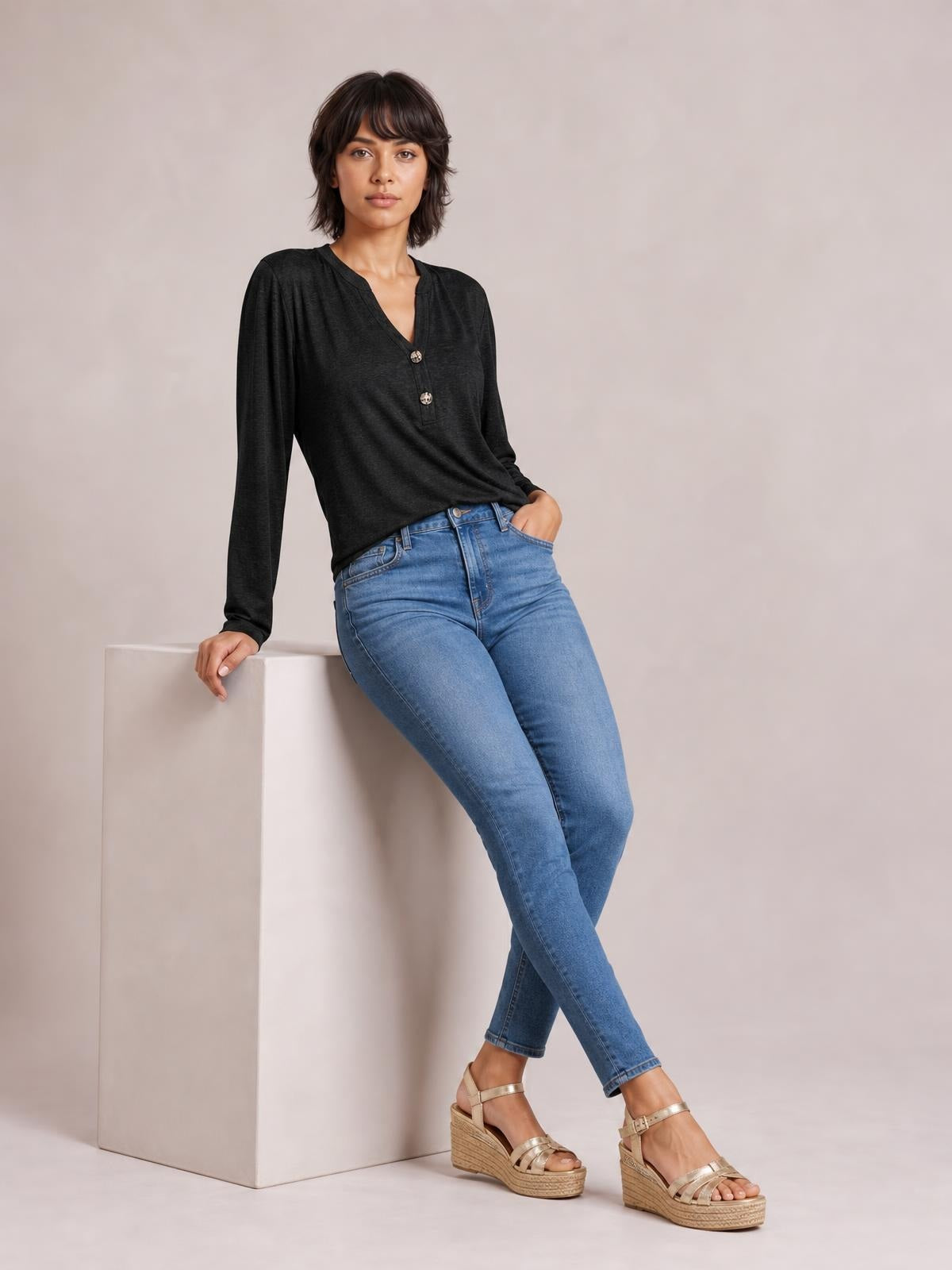 Model seated in a black notched long sleeve T-shirt with a relaxed silhouette, V-neckline, and two-button placket, paired with blue jeans.