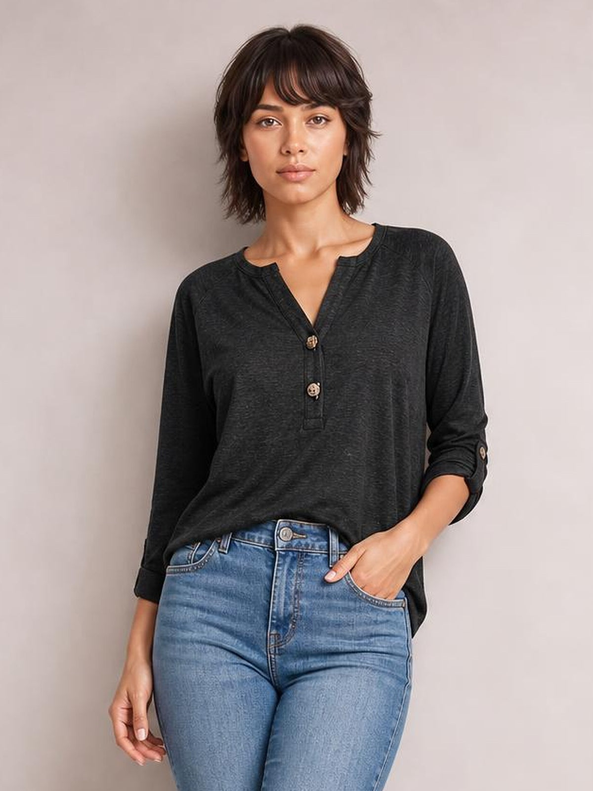 Model wearing a charcoal notched long sleeve T-shirt with a relaxed silhouette, buttoned placket, and rolled sleeves, posing with one hand in her jeans pocket.