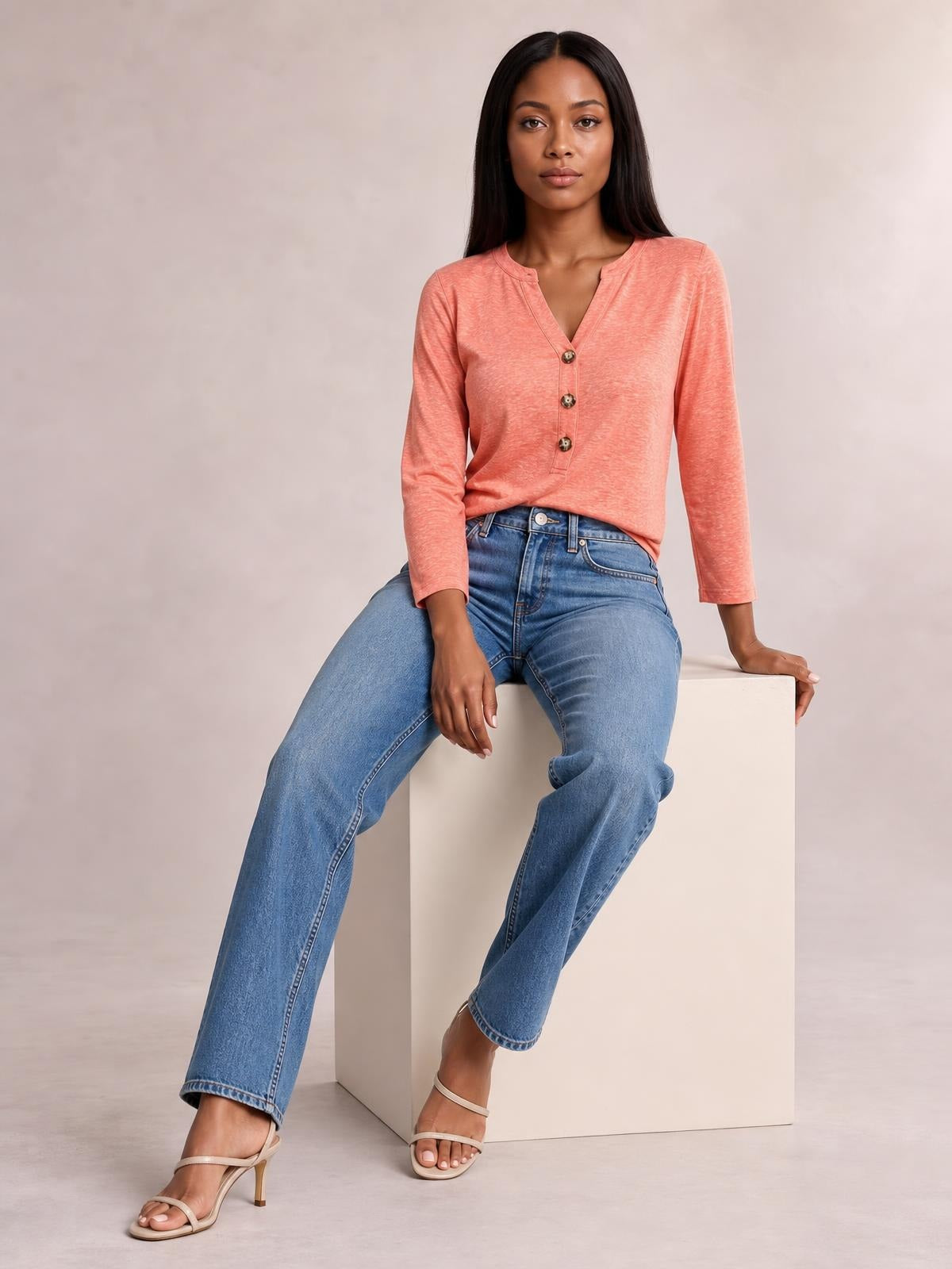 Model seated in a coral notched long sleeve T-shirt with a relaxed silhouette, V-shaped neckline, and three-button front placket.