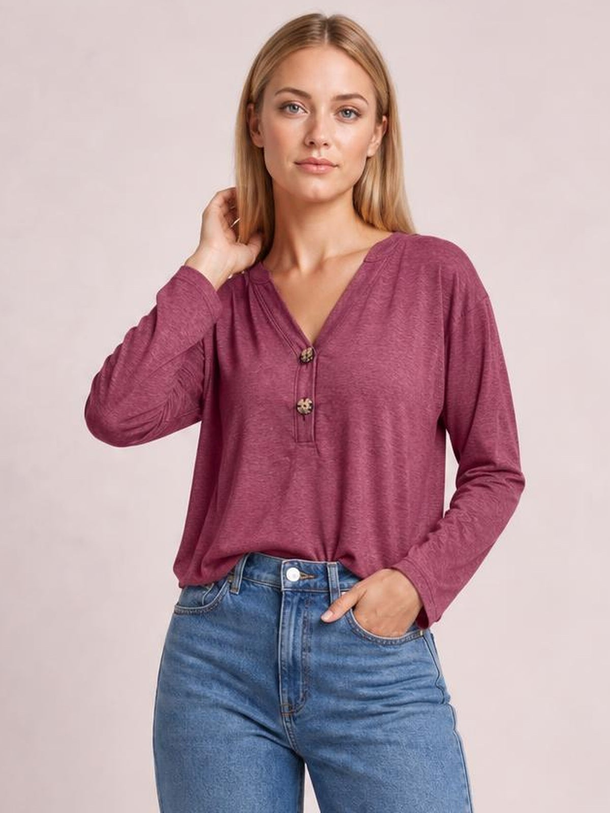 Model wearing a burgundy notched long sleeve T-shirt with a relaxed silhouette, V-neckline, and two-button placket, posing with one hand in her jeans pocket.