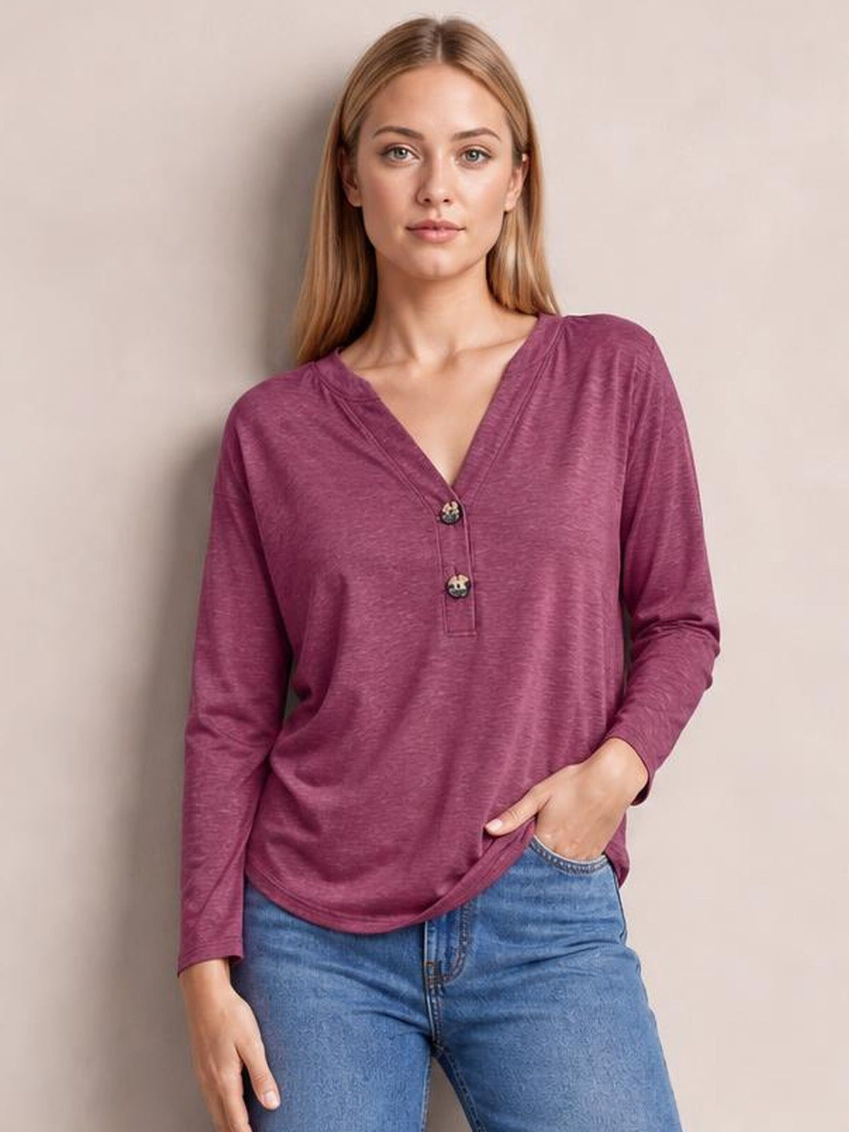 A woman poses in a burgundy notched long sleeve T-shirt with a relaxed silhouette, V-neckline, and two decorative front buttons.