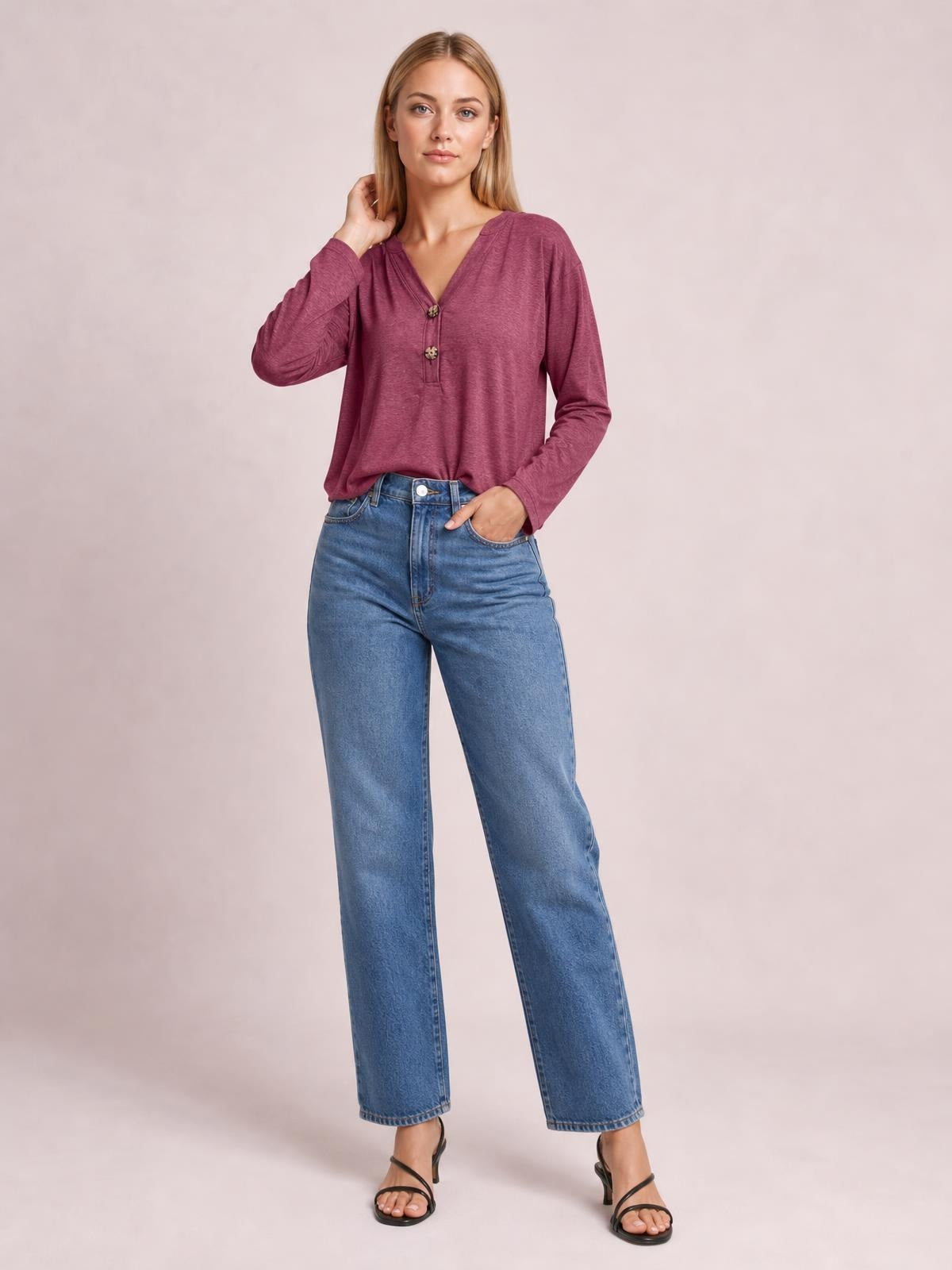 Model wears a burgundy notched long sleeve T-shirt with a relaxed silhouette and two-button front, posing with one hand at her neck and the other in a pocket.