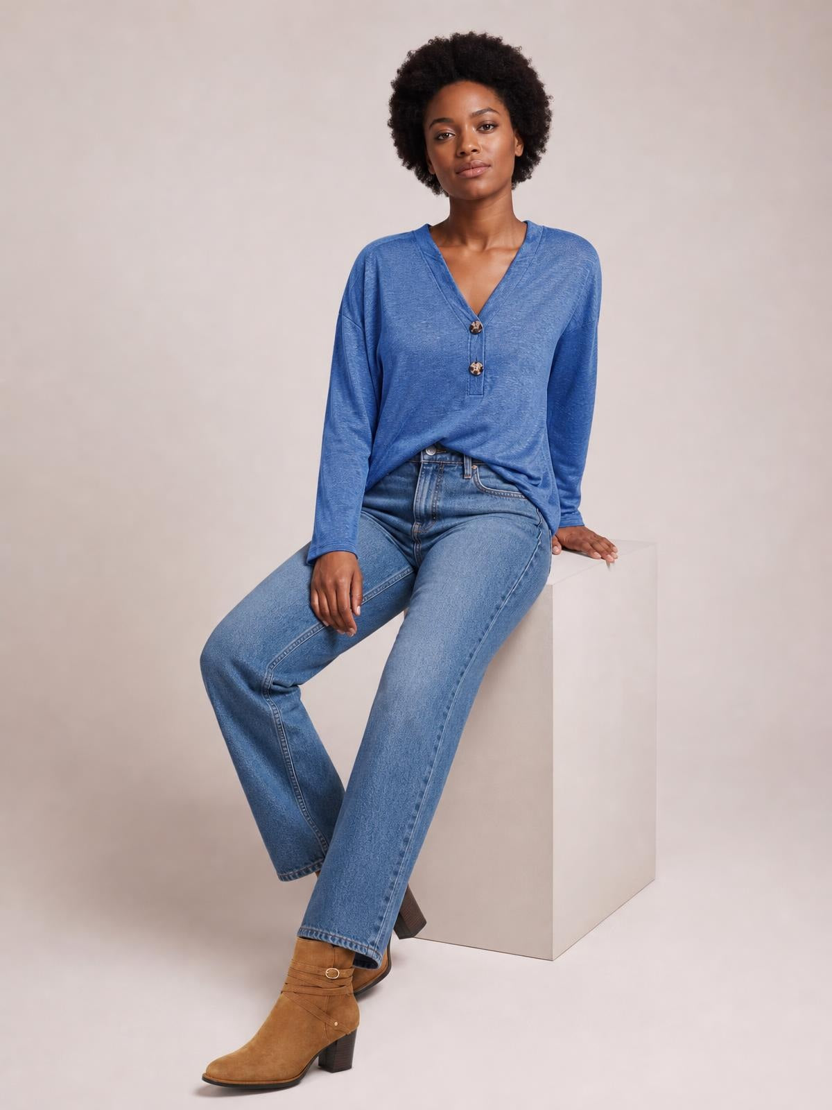 Model seated in a blue notched long sleeve T-shirt with a relaxed silhouette, V-neckline, and two-button placket.