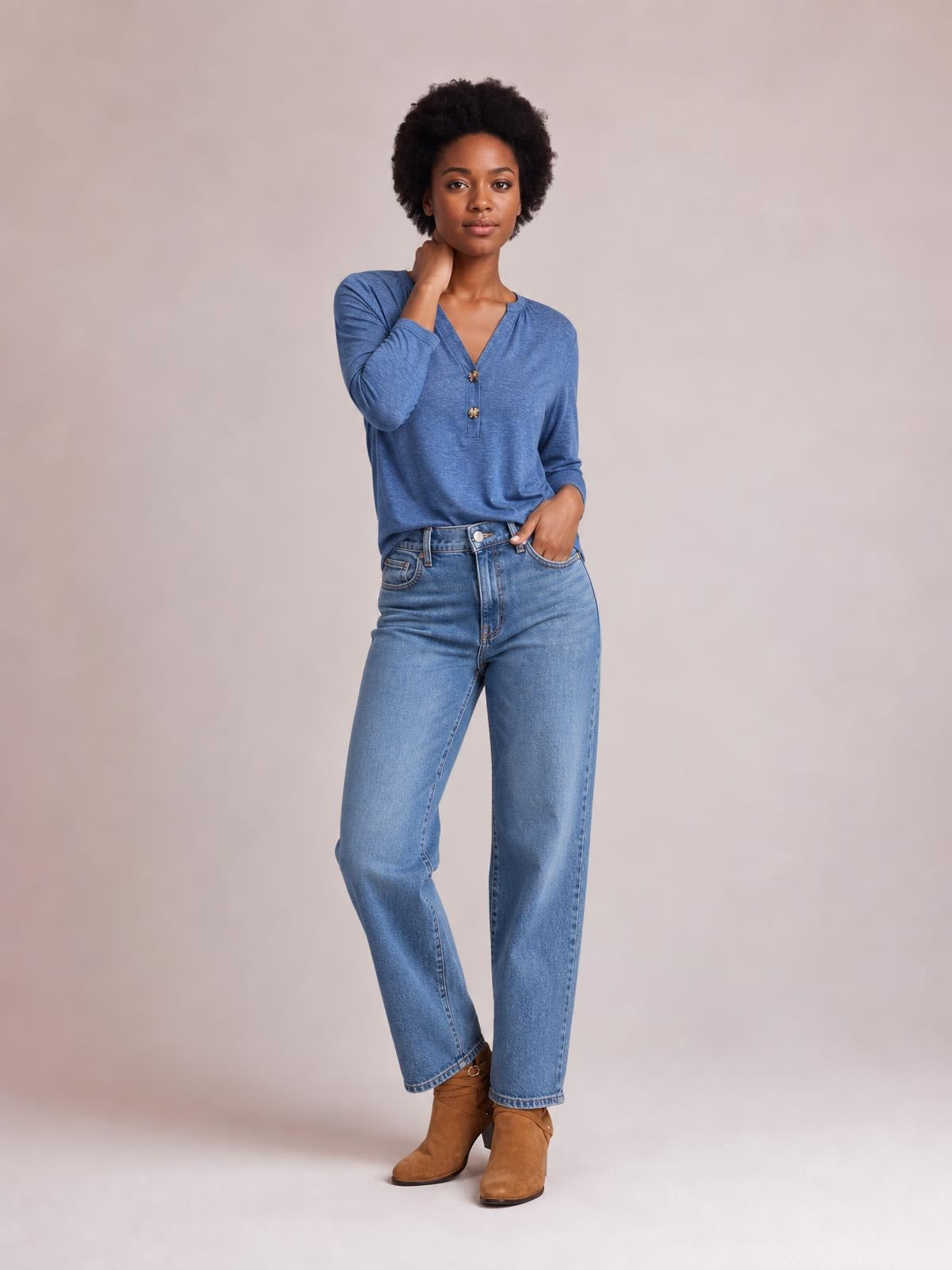 Model wearing a blue notched long sleeve T-shirt with a relaxed silhouette, V-neckline, and two-button placket, posing with one hand at her neck.