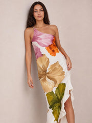 Model poses in a white satin floral print maxi dress with pink, orange, and olive blooms, an asymmetric one-shoulder neckline, fitted silhouette, and ruffled hem.