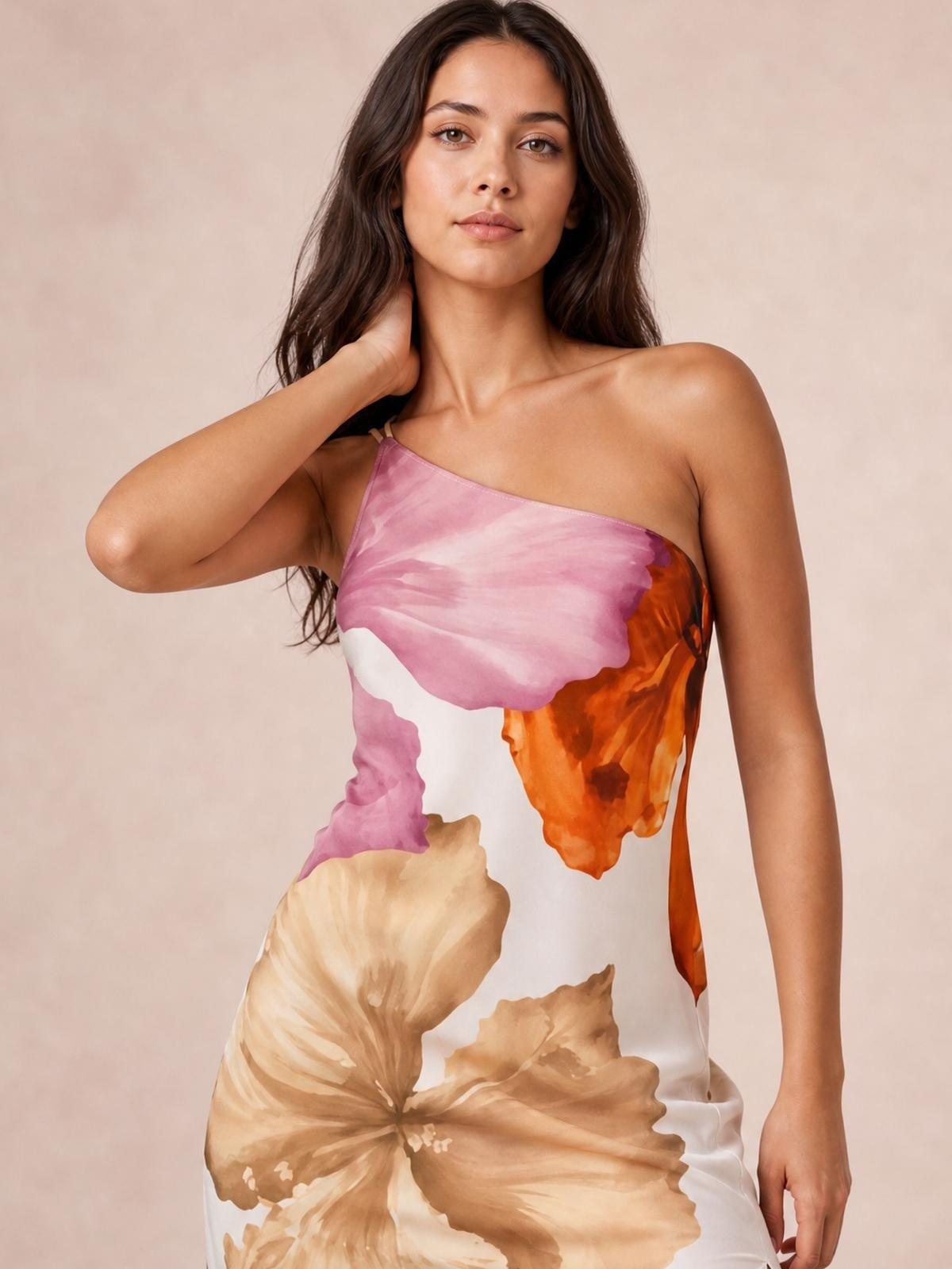 Model poses with one hand at her neck in a pink, orange, beige, and white floral-print satin maxi dress with a one-shoulder neckline.