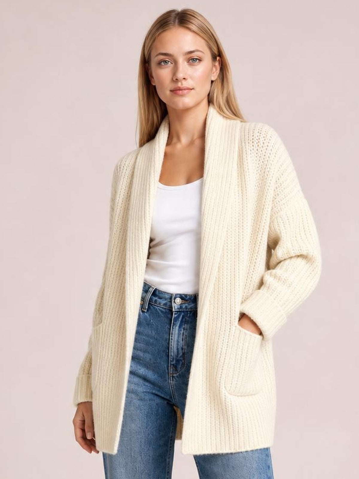 Model wears an ivory open-front ribbed cardigan with long sleeves, a relaxed silhouette, and large patch pockets over a white top and jeans.