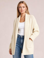 Model wears an ivory open-front ribbed cardigan with long sleeves, a relaxed silhouette, and large patch pockets over a white top and jeans.