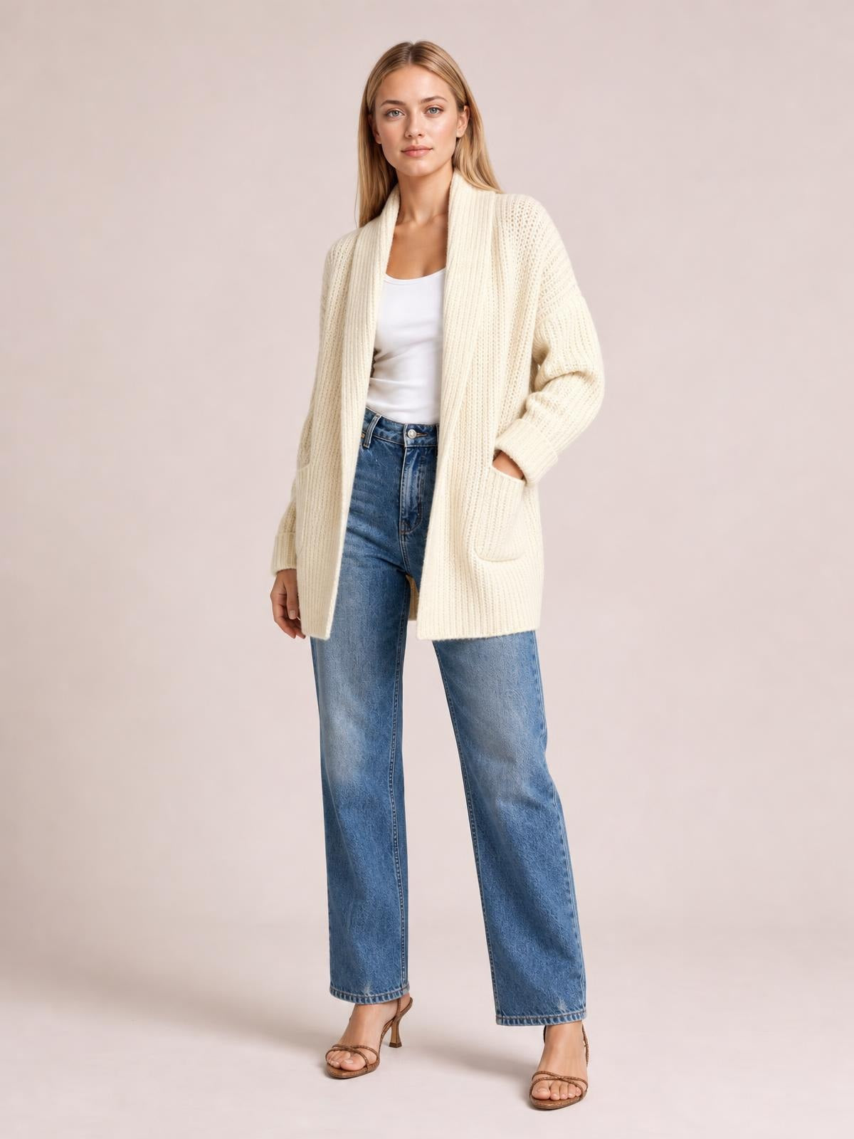 A model wears an ivory ribbed open-front cardigan with a relaxed long silhouette and front pockets over a white top and blue jeans.
