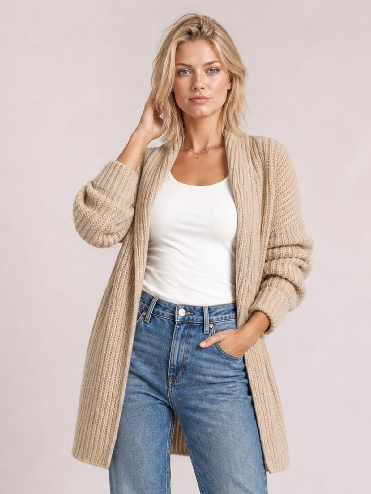 Blonde model wearing a beige ribbed open-front cardigan with long sleeves and pockets, layered over a white top with one hand in a pocket.
