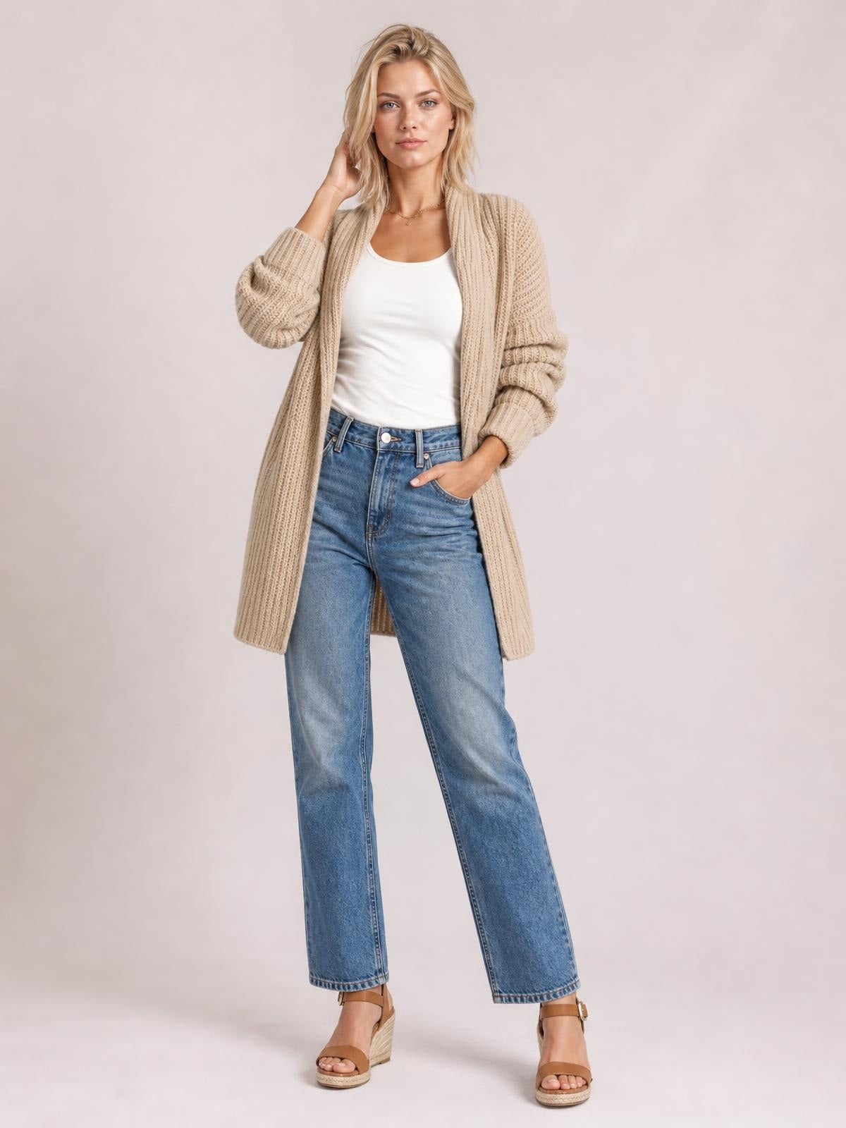 Model wears a beige ribbed open-front cardigan with long sleeves, a relaxed longline silhouette and pockets, posing with one hand in her jeans pocket.