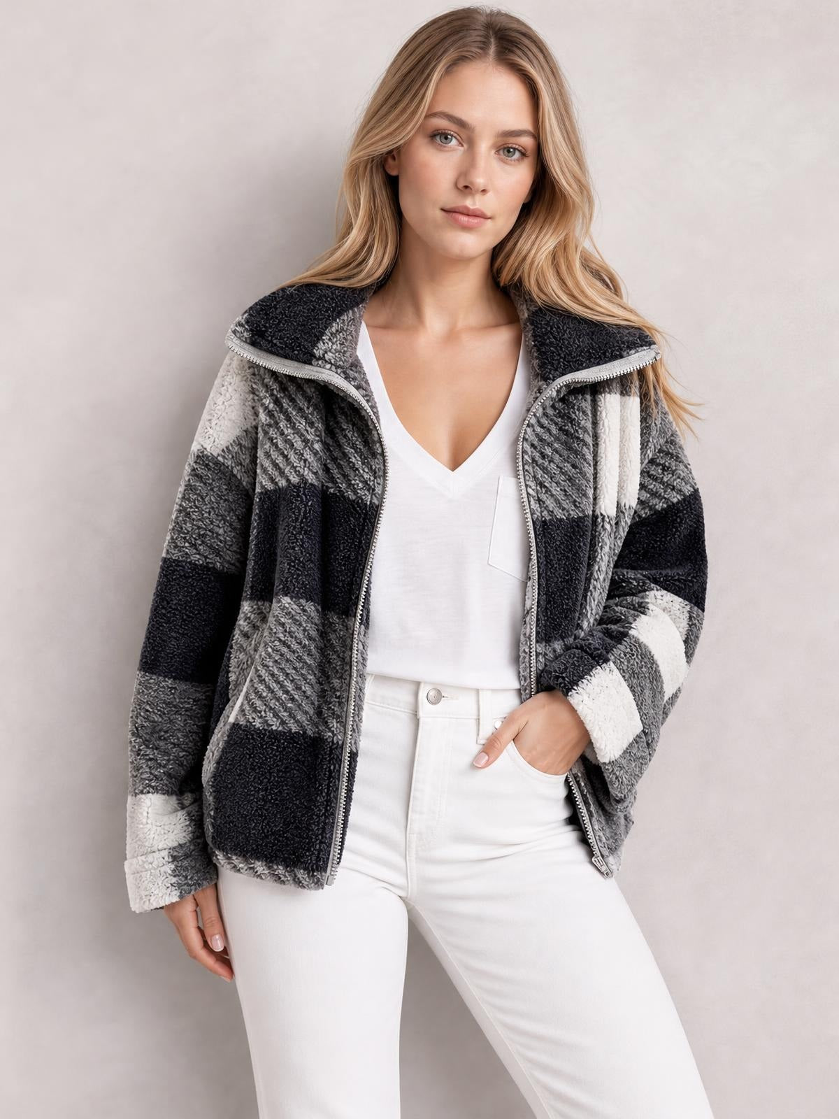 A woman stands with one hand in her pocket, wearing a black, gray, and white plaid zip-up jacket with long sleeves, a relaxed silhouette, and front pockets.