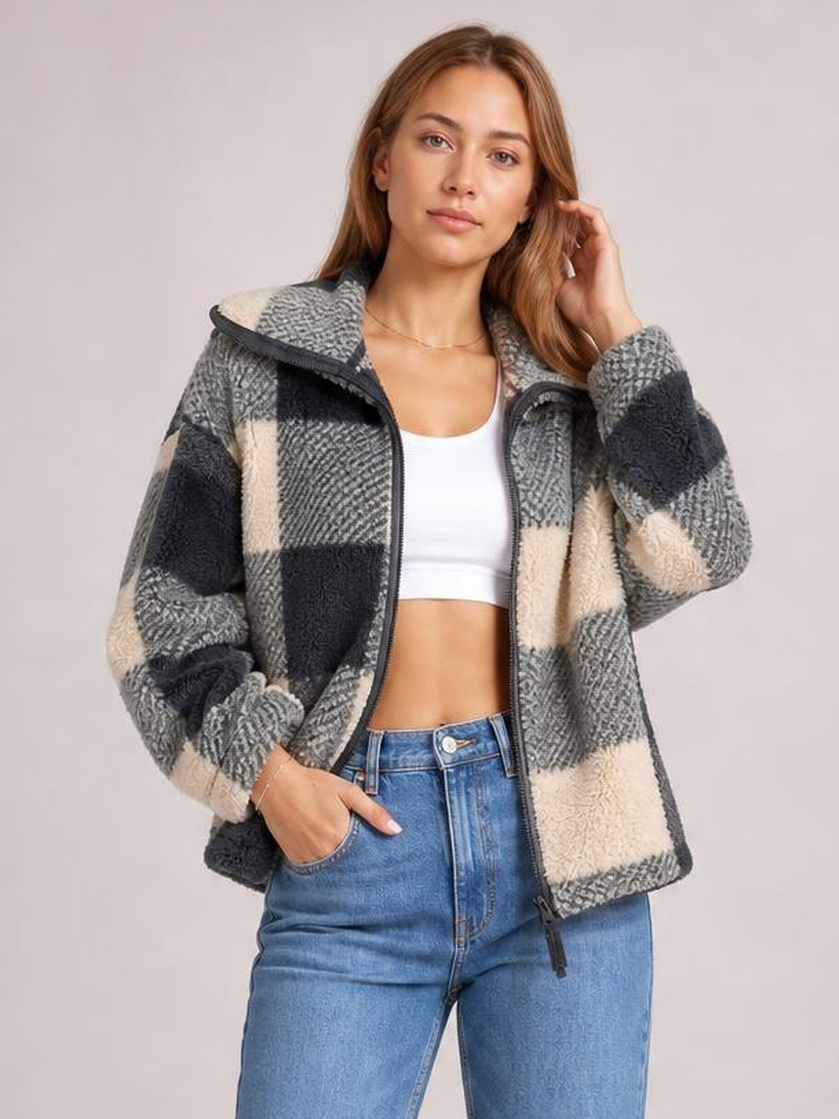 A model wears a gray, black, and cream plaid zip-up long-sleeve jacket with a relaxed silhouette, front zipper, and hands in the pockets.
