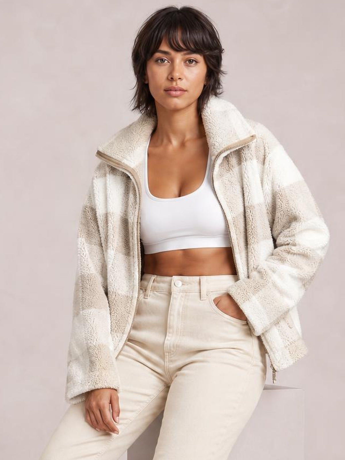 Model wears a cream zip-up long sleeve jacket with a plush textured finish, relaxed oversized silhouette, and high collar, posed with one hand in a pocket.