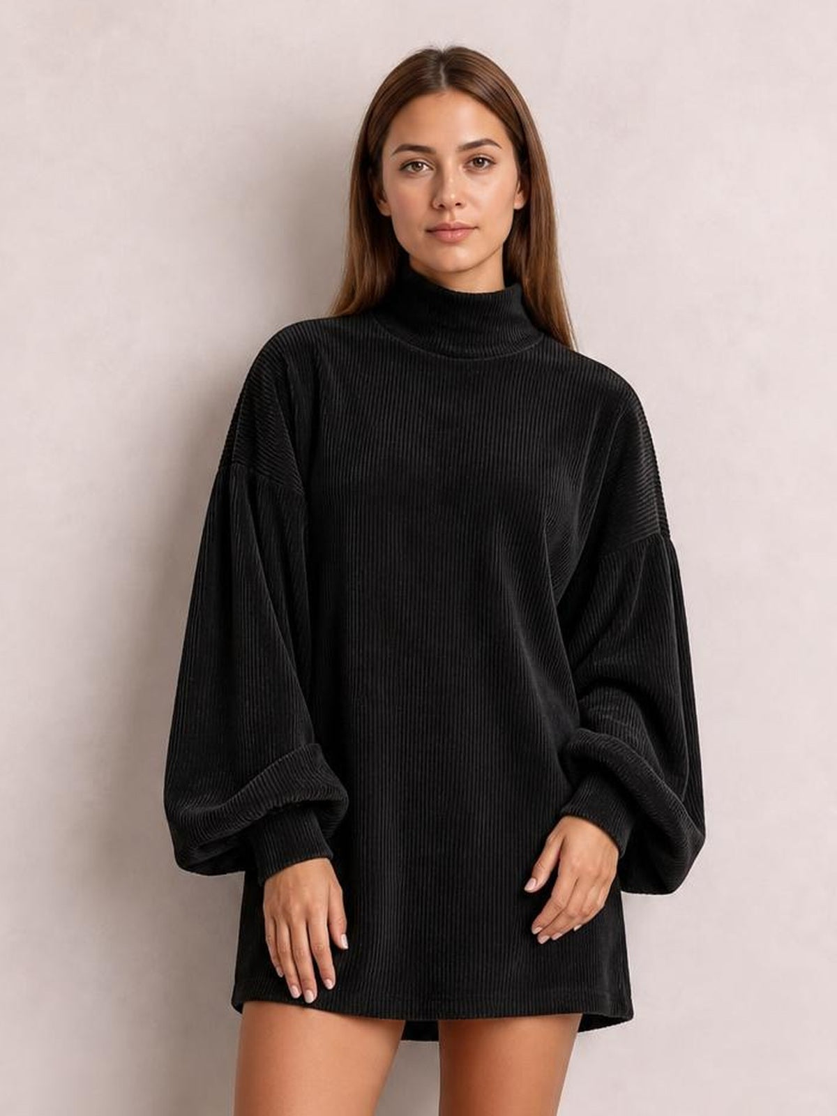 Model stands facing forward in a black ribbed mock neck mini dress with a relaxed silhouette, oversized lantern sleeves, and fitted cuffs.