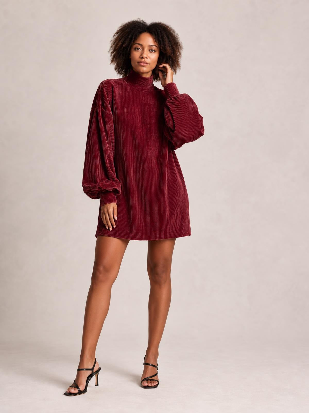 Model poses in a burgundy ribbed mock neck mini dress with a loose straight silhouette, lantern sleeves, gathered cuffs, and stretch texture.