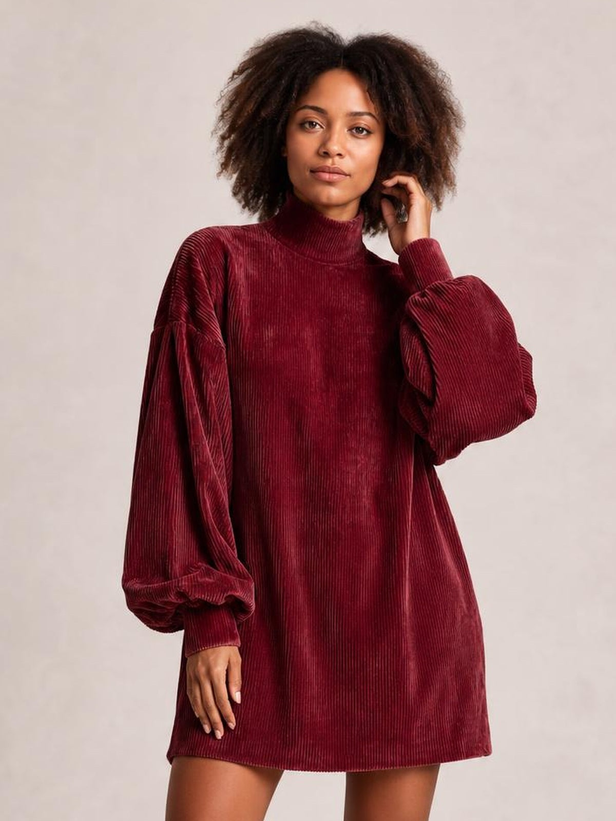 A model poses in a burgundy ribbed mock neck mini dress with a relaxed straight silhouette and voluminous lantern sleeves with fitted cuffs.