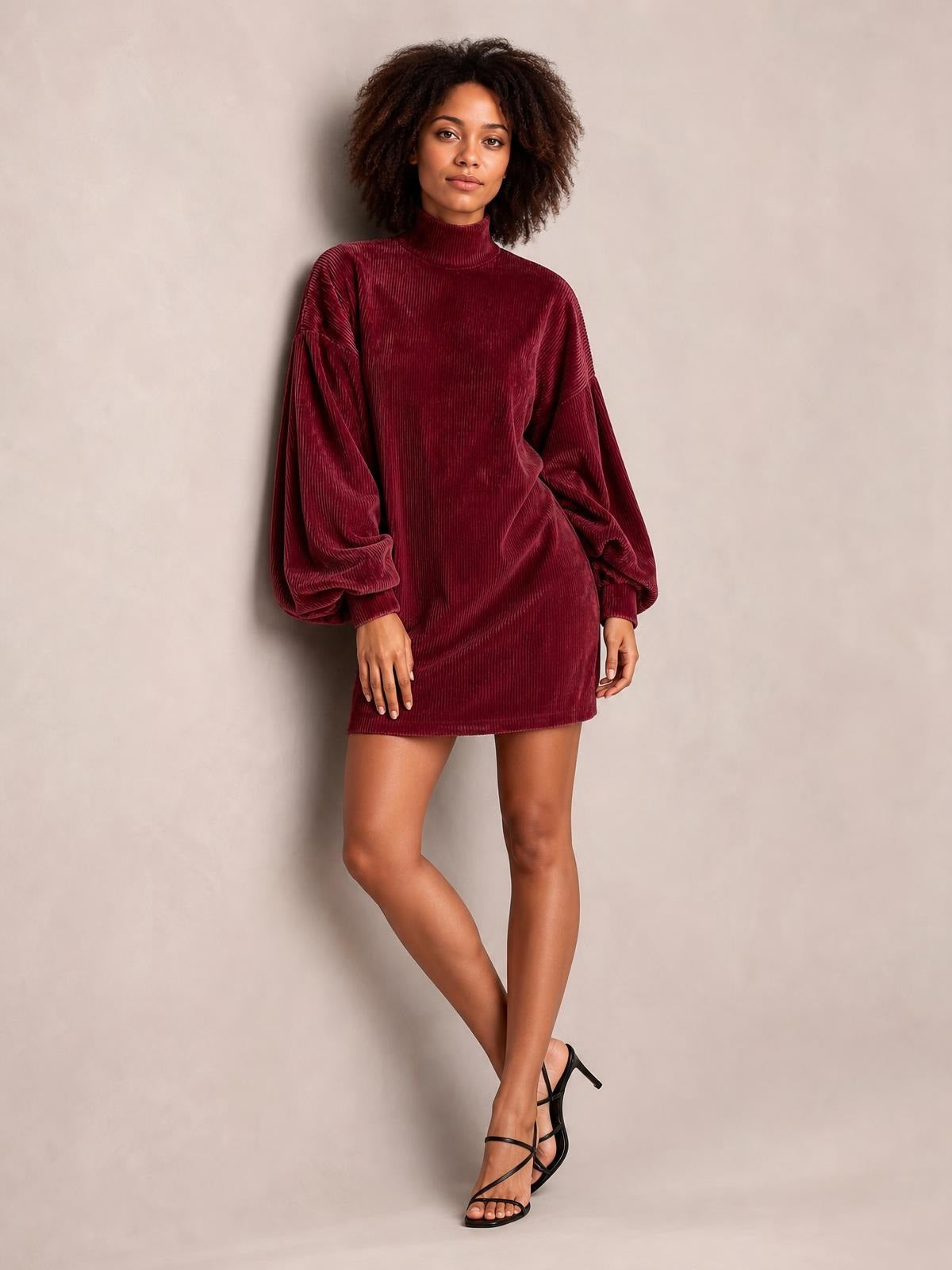 A model poses with crossed legs in a burgundy ribbed mock-neck mini dress featuring voluminous lantern sleeves and a relaxed straight silhouette.