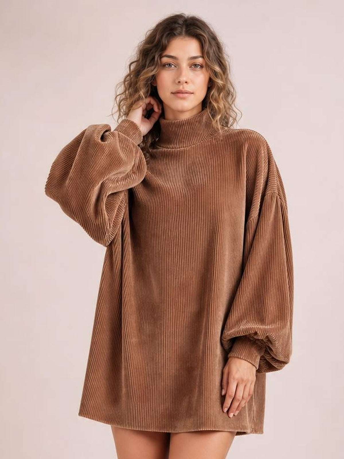Model in a brown ribbed mock neck mini dress with a relaxed straight silhouette and voluminous lantern sleeves, posing with one hand near her hair.
