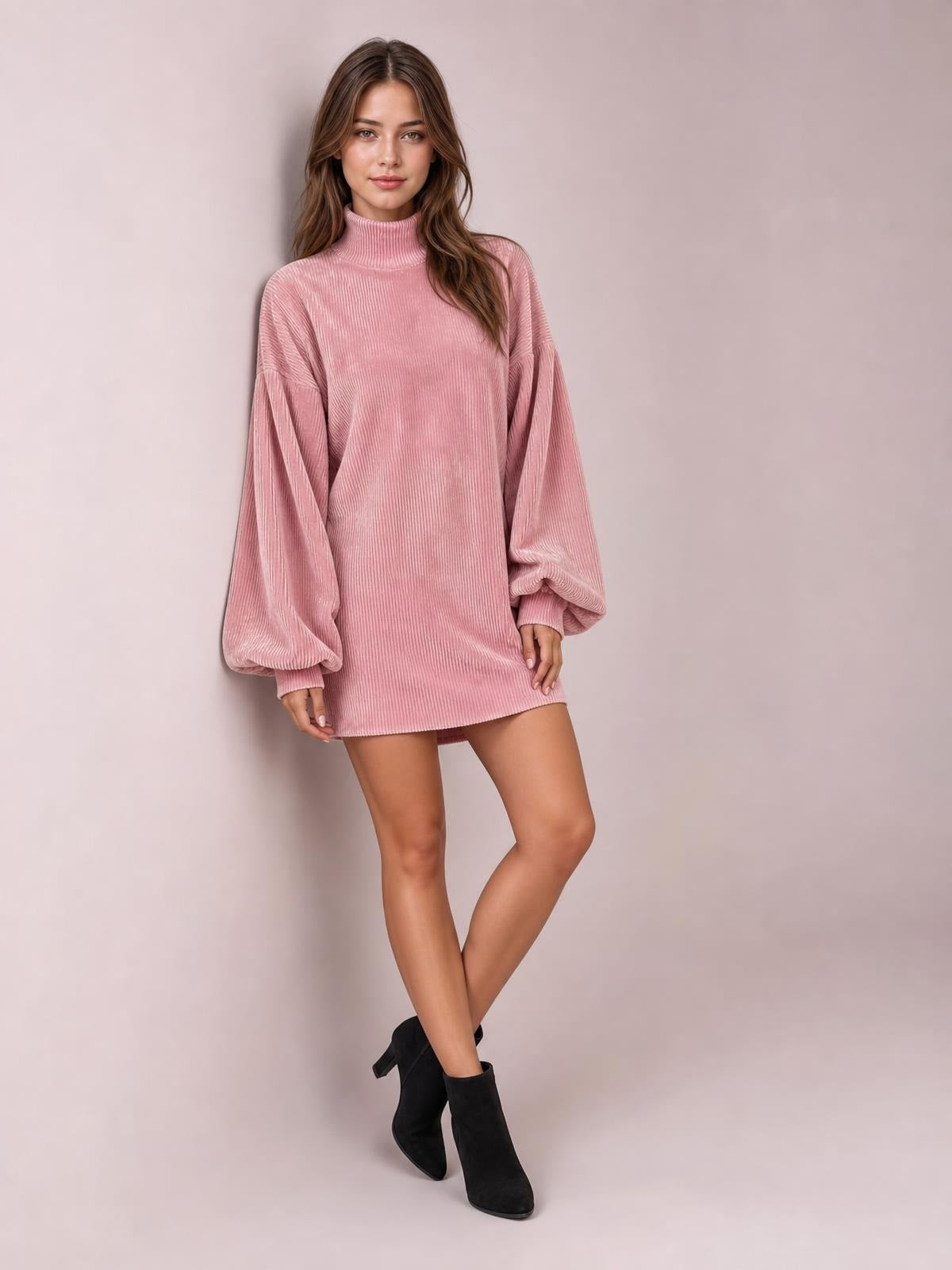 Model in a pink ribbed mock neck mini dress with voluminous lantern sleeves, gathered cuffs, and a relaxed straight silhouette, posed with crossed legs.