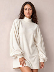 A model poses in a cream ribbed mock neck mini dress with a relaxed silhouette, long lantern sleeves, and fitted ribbed cuffs.