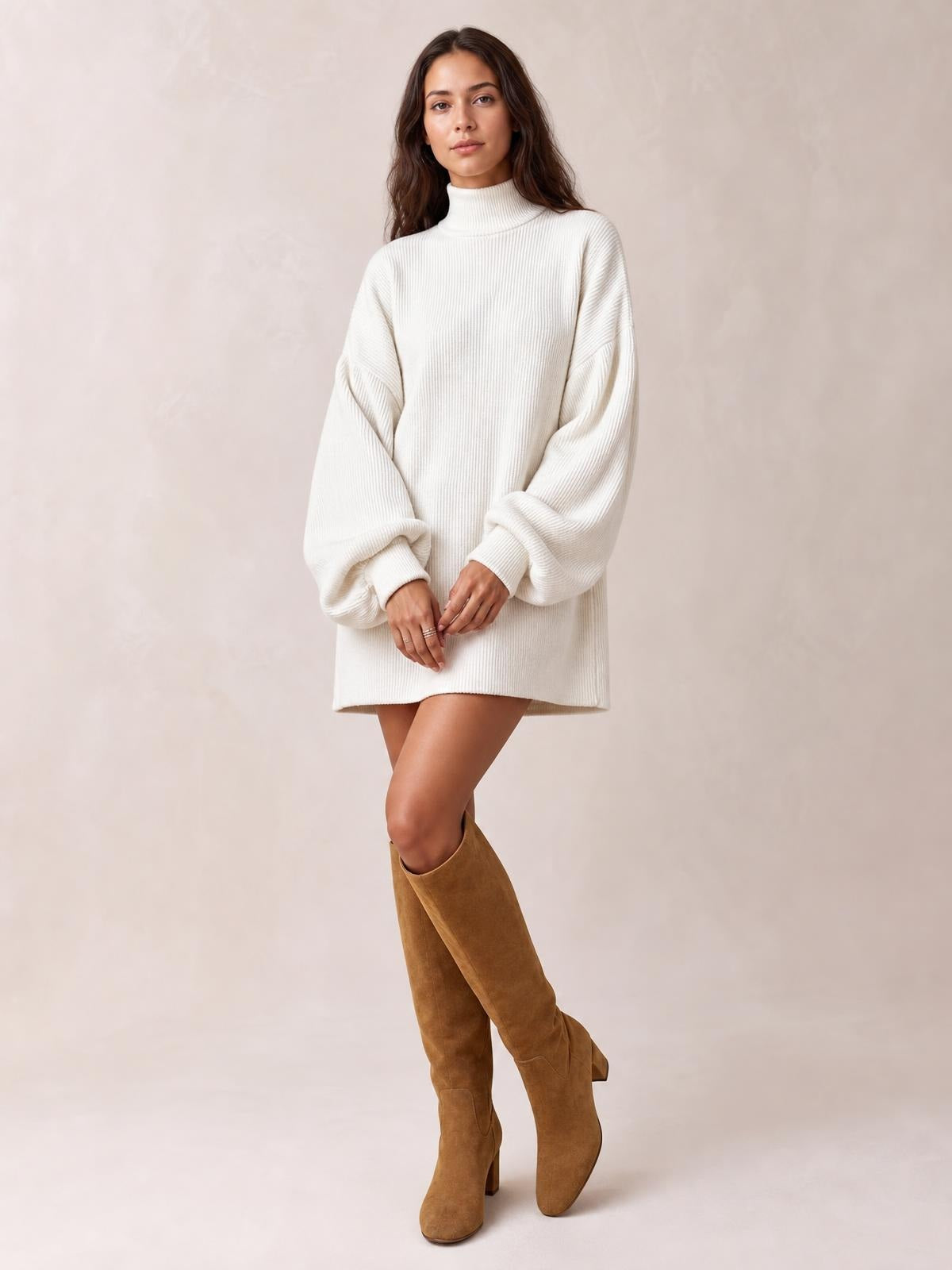 A model stands with hands clasped and legs crossed in a white ribbed mock neck mini dress with a relaxed silhouette and voluminous lantern sleeves.