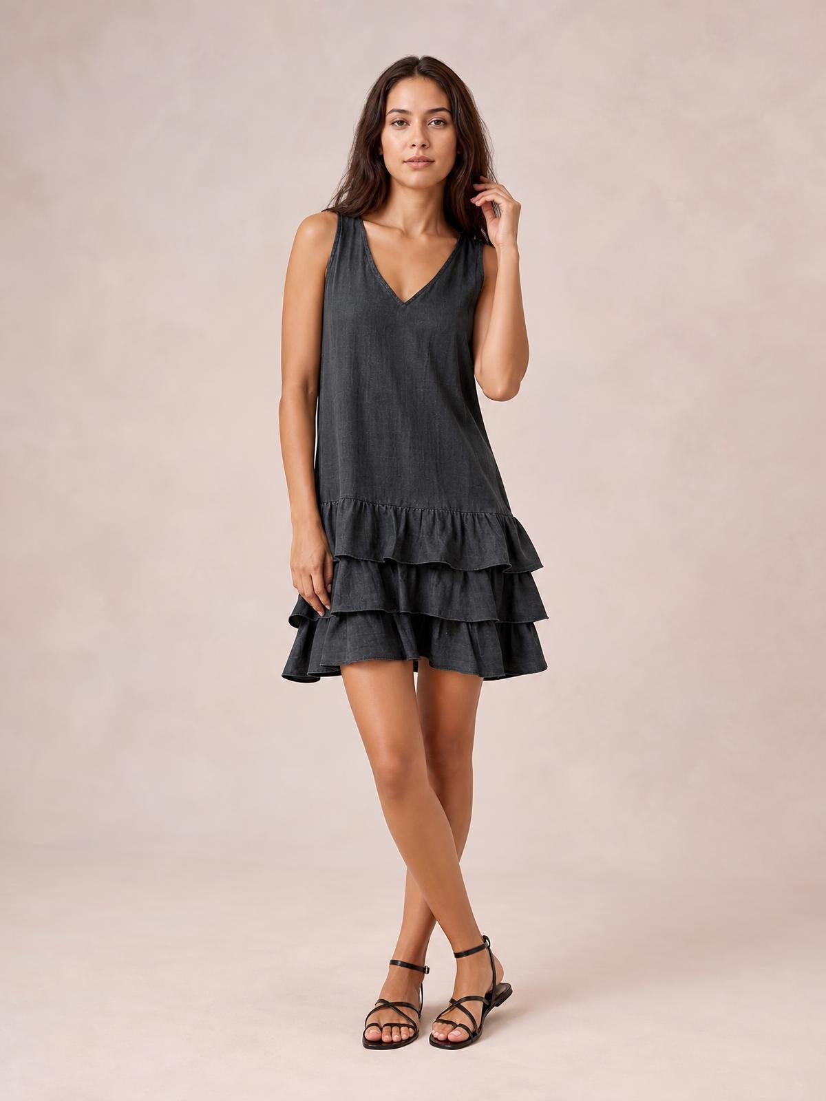 Model poses in a charcoal gray sleeveless V-neck dress with a loose silhouette, tiered construction, and multiple ruffled hems.