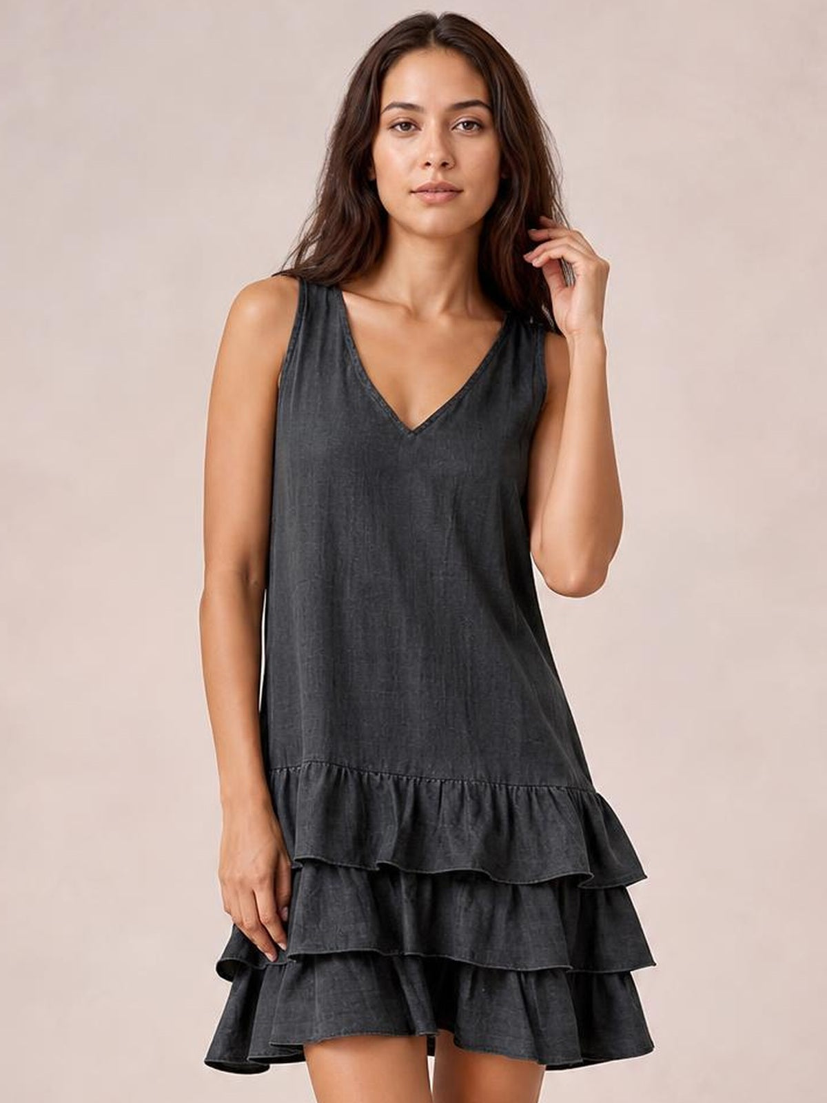 Model poses in a charcoal sleeveless V-neck dress with a relaxed silhouette and three-tiered ruffled hem.