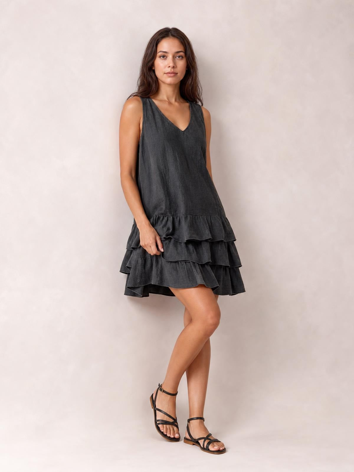 Model poses in a dark charcoal sleeveless V-neck dress with a loose silhouette and multiple tiered ruffled hems.