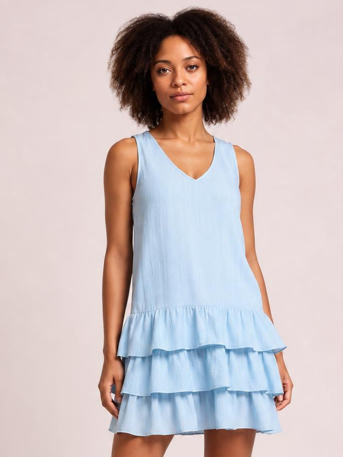 A model stands in a light blue plus-size sleeveless V-neck dress with a relaxed silhouette and multiple tiered ruffled hem layers.