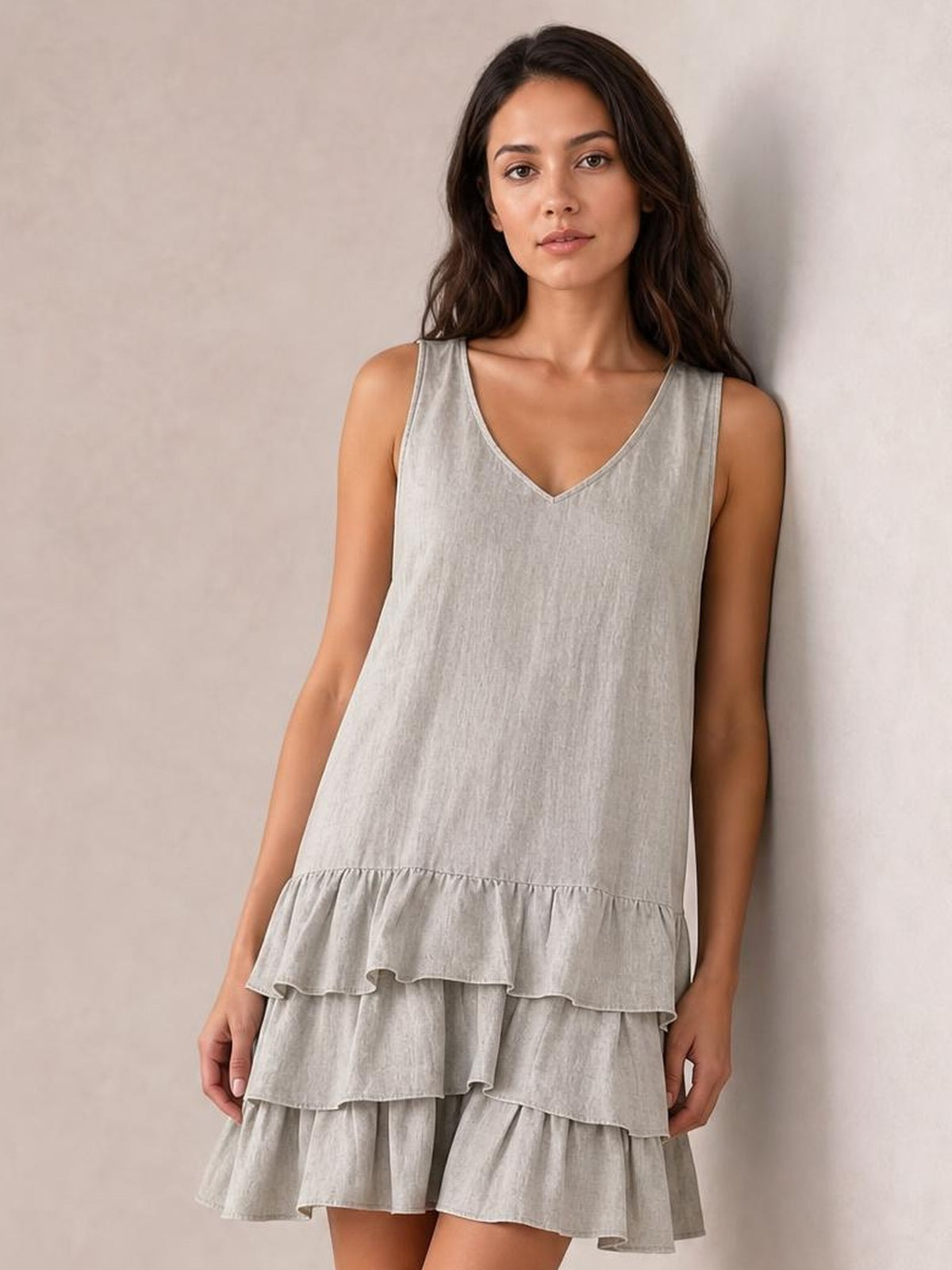 Model wears a light gray plus-size sleeveless V-neck dress with a relaxed silhouette and multiple tiered ruffled hem layers, standing with hands at her sides.