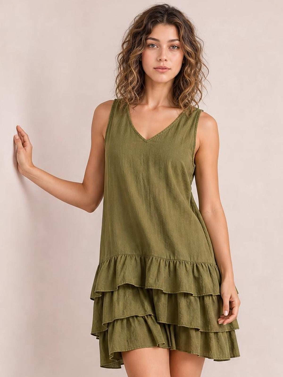 Model poses with one hand raised in an olive green sleeveless V-neck dress featuring a relaxed silhouette and multiple tiered ruffled hems.