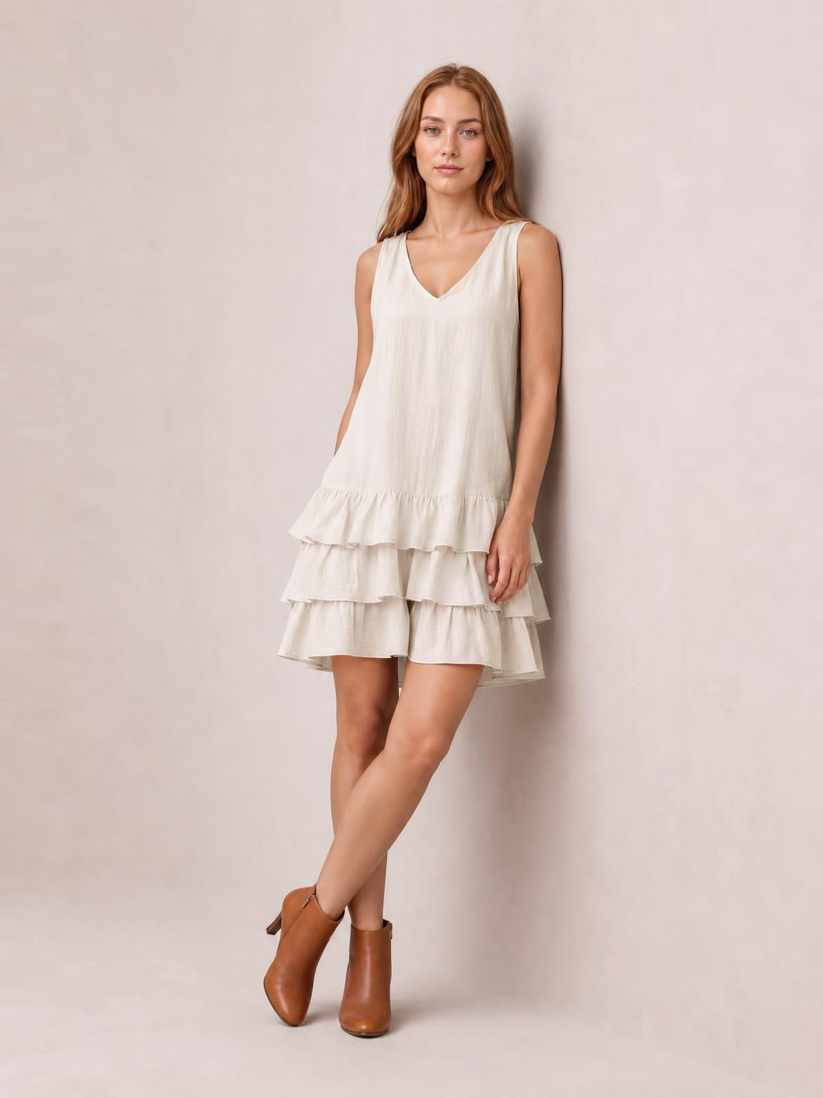Model stands with crossed legs in a cream sleeveless V-neck dress featuring a relaxed silhouette and tiered ruffled hem.