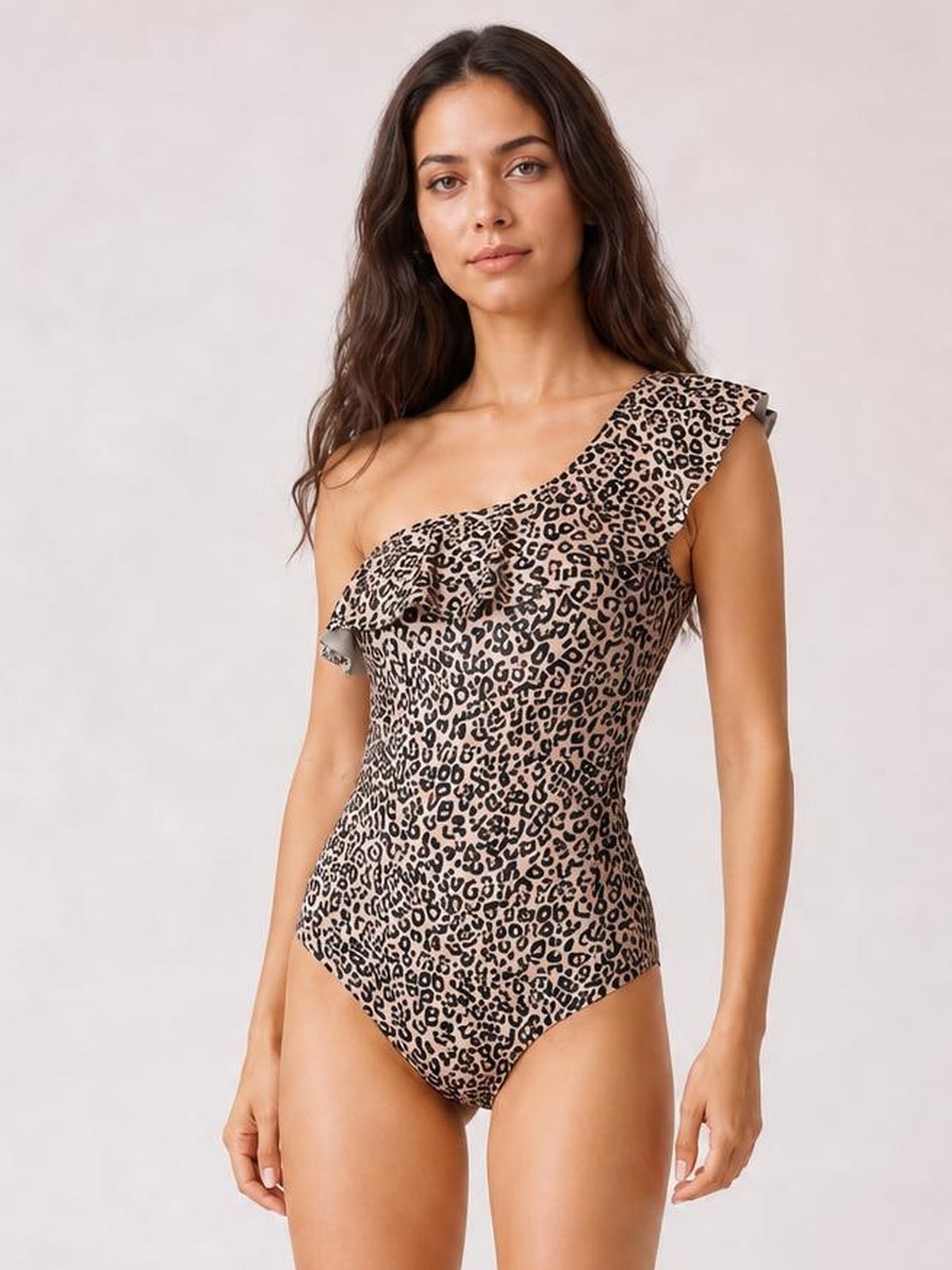 Model poses in a leopard-print one-piece swimsuit with a single shoulder strap, ruffled neckline, and fitted high-cut silhouette.