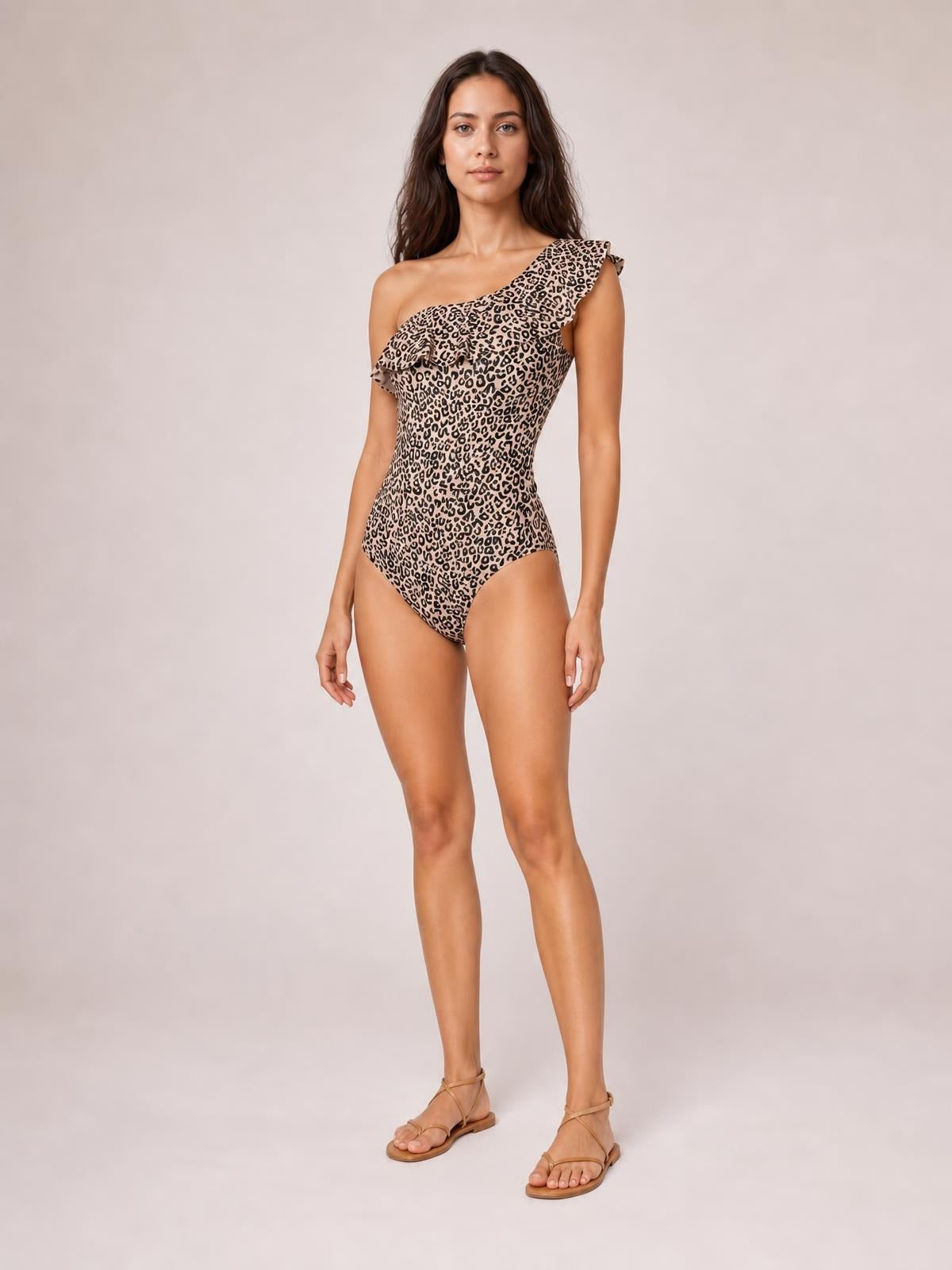 Model stands in a relaxed pose wearing a leopard-print one-piece swimsuit with a single shoulder, ruffled neckline, and fitted high-cut silhouette.