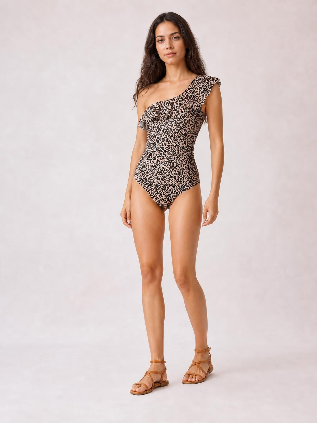Model stands in a leopard-print one-piece swimsuit with a single shoulder, ruffled neckline, and fitted silhouette.