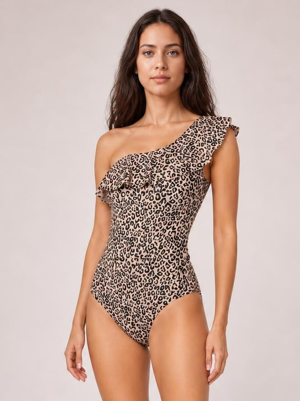 Model stands facing forward in a leopard-print one-piece swimsuit with a single shoulder, ruffled neckline, fitted silhouette, and high-cut leg.