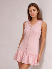 A model poses in a pink sleeveless mini dress with a ruffled neckline, button-front construction, straight bodice, and gathered flounce hem.