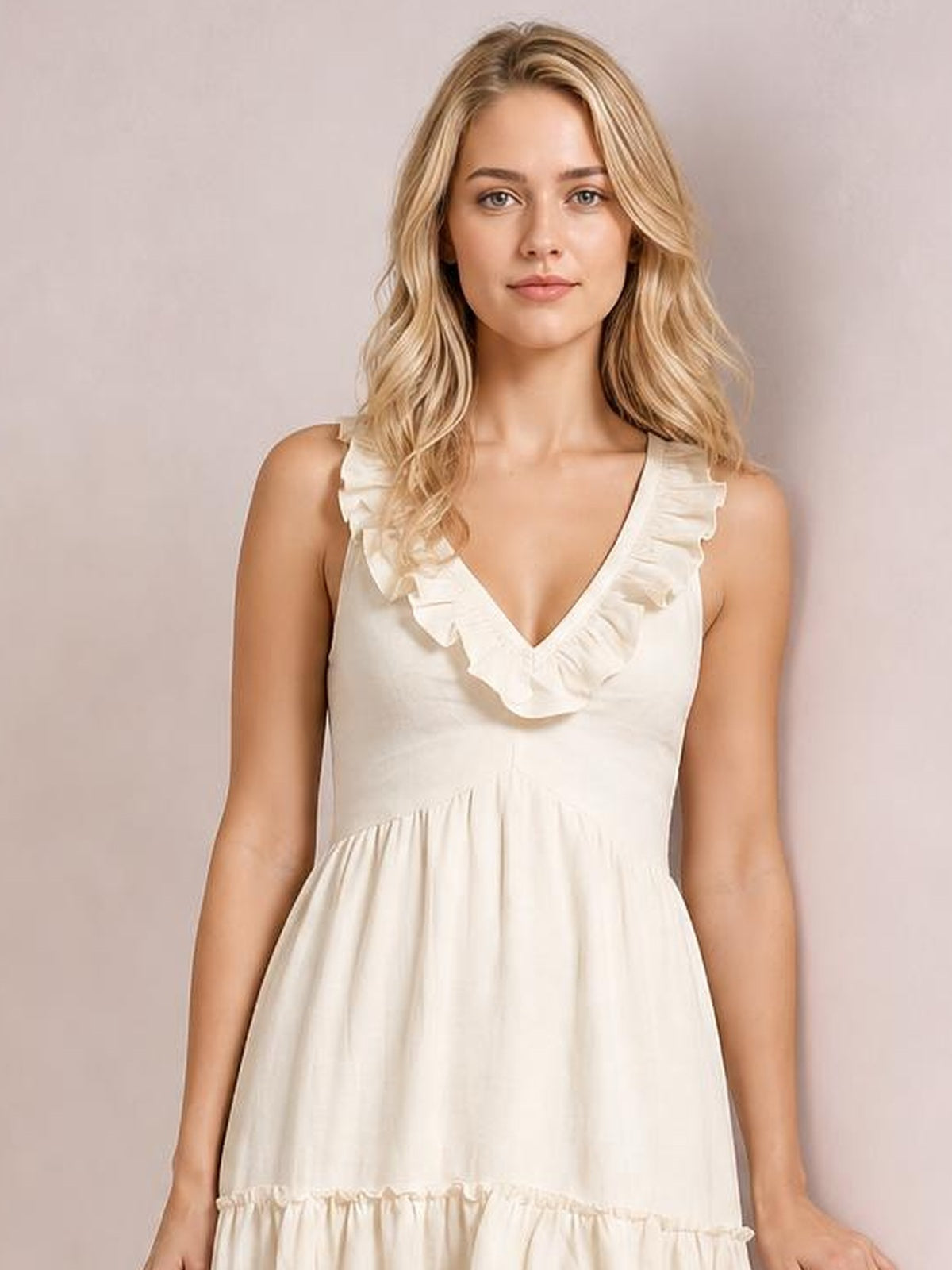 A model faces forward in an ivory plus-size midi dress with a deep V-neck, ruffled shoulder trim, gathered waist, and tiered flowing skirt.