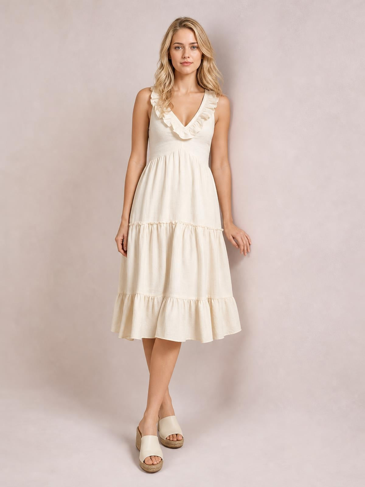 Model poses in a cream ruffled V-neck tiered midi dress with a fitted bodice, gathered waist, and flowing A-line silhouette.