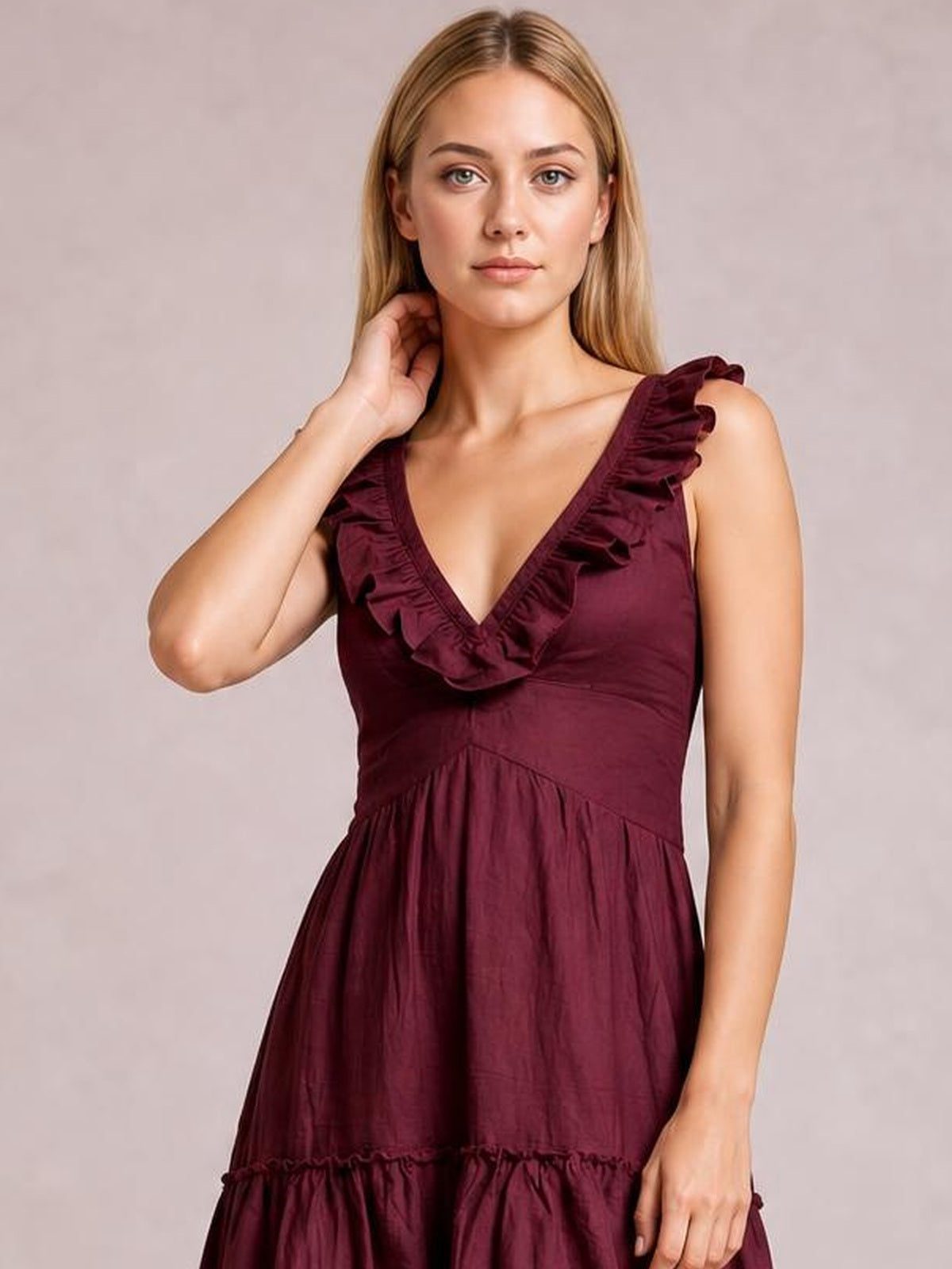 A model poses in a burgundy ruffled V-neck midi dress with wide shoulder ruffles, a fitted waist, and a flowing tiered silhouette.
