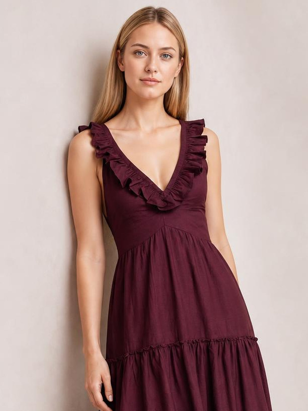 Model wears a burgundy ruffled V-neck midi dress with sleeveless shoulders, a gathered waist, and a tiered, flowing skirt.