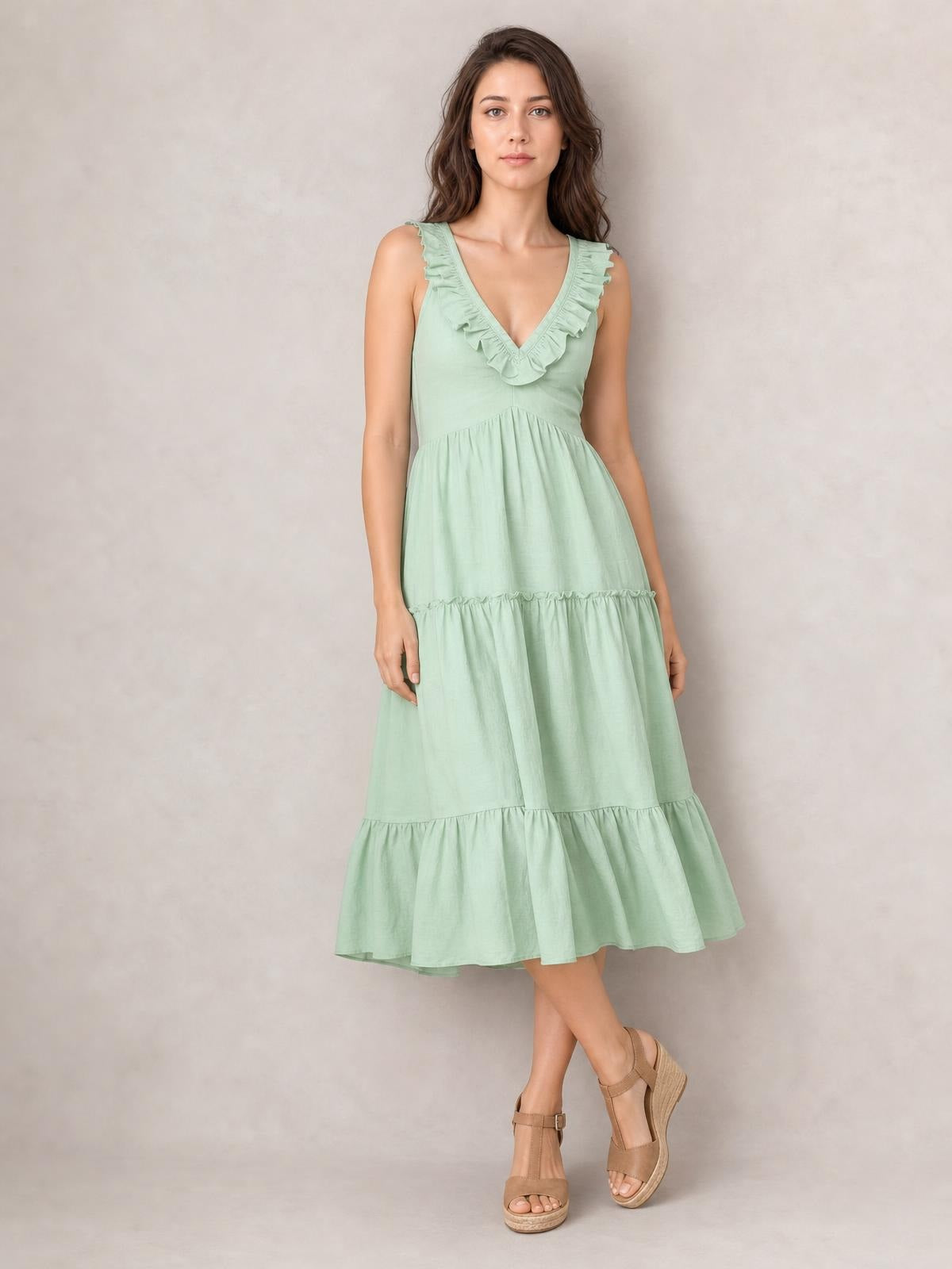 Model poses with crossed legs in a mint green tiered midi dress featuring a deep V-neck, ruffled trim, gathered waist, and flowing A-line silhouette.