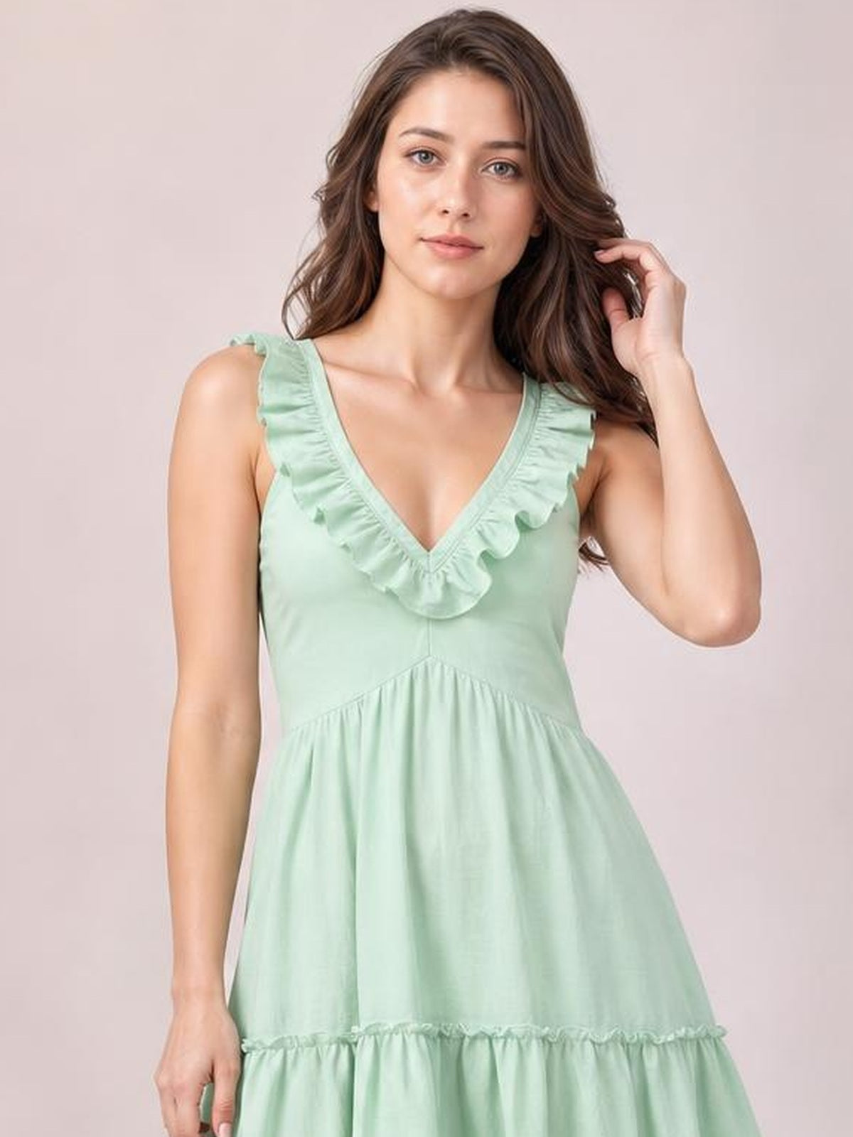 A model poses in a mint green sleeveless V-neck midi dress with ruffled trim, a gathered waist, tiered skirt, and relaxed A-line silhouette.