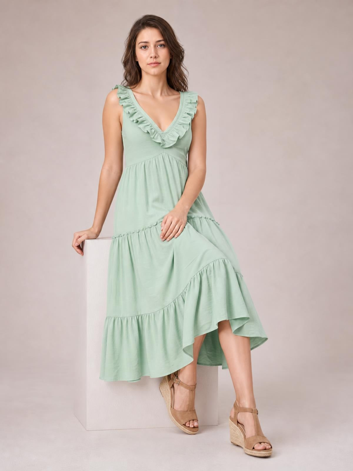 A model poses in a mint green ruffled V-neck midi dress with sleeveless styling, gathered tiers, and a flowing A-line silhouette.