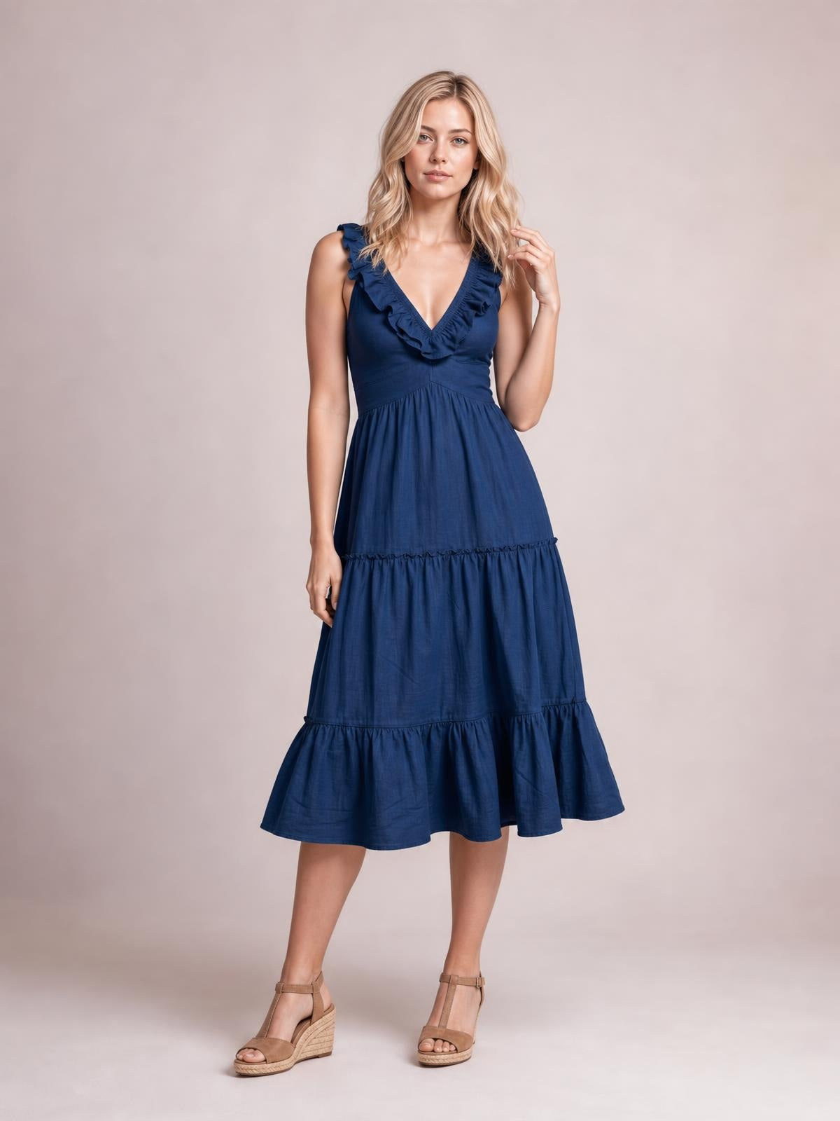 Model poses in a navy blue ruffled V-neck midi dress with a fitted waist, tiered flowing skirt, and flared silhouette.