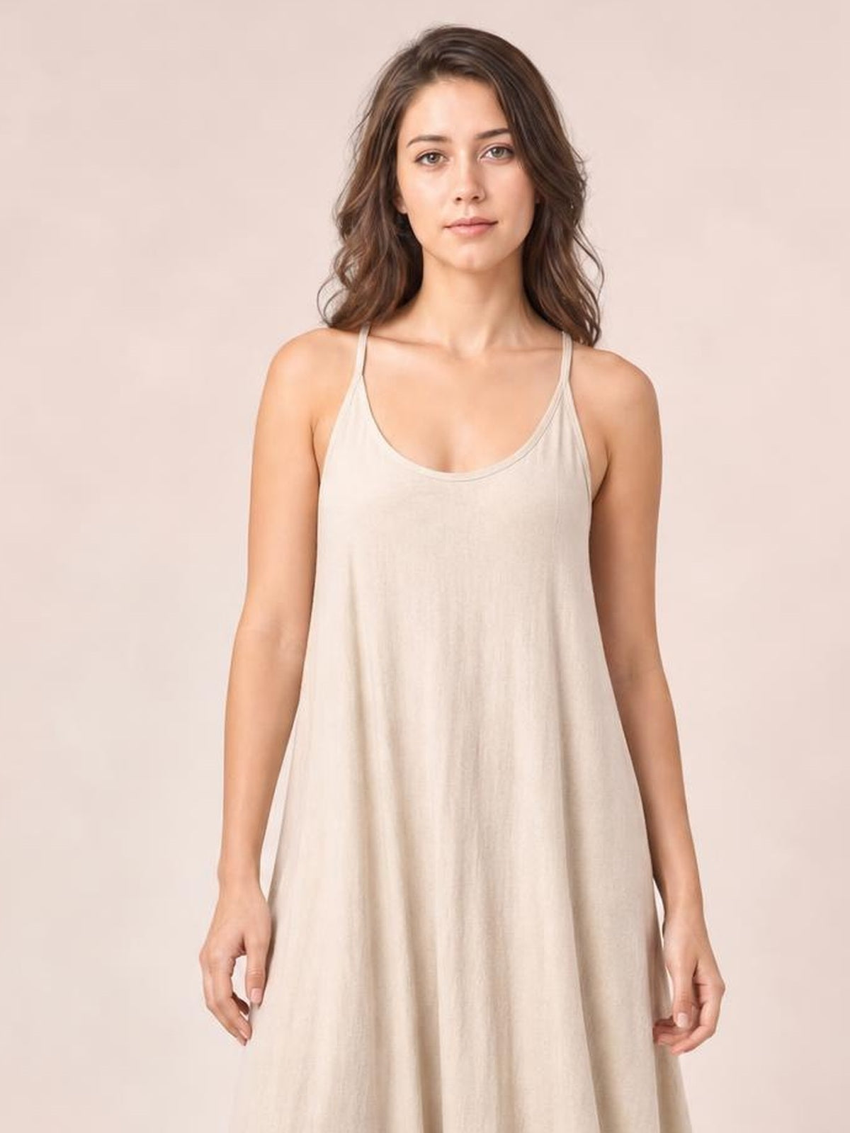 Model standing in a light beige scoop-neck spaghetti-strap maxi dress with a relaxed, flowing A-line silhouette and softly draped construction.