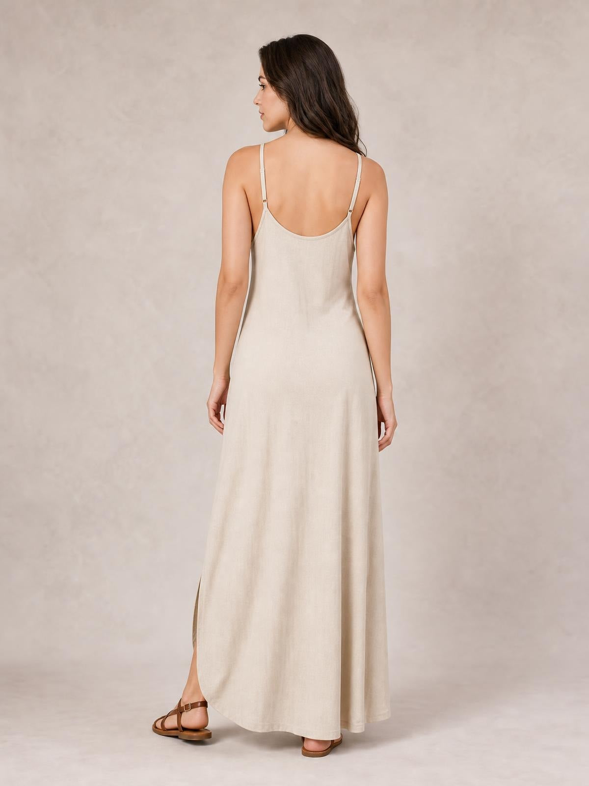 Model shown from behind in a cream plus-size maxi dress with thin spaghetti straps, a scoop back, relaxed floor-length silhouette, and side slit.