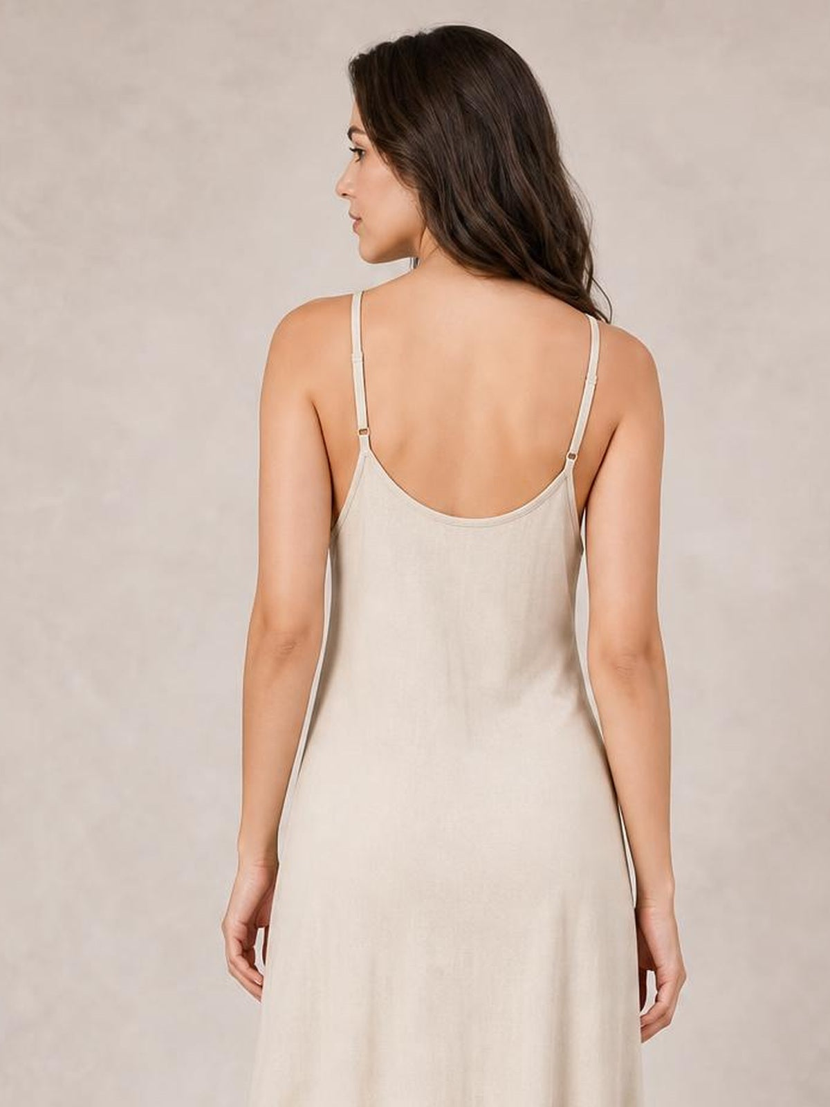 A model stands facing away in a cream scoop neck spaghetti strap maxi dress with a relaxed, flowing silhouette and adjustable back straps.